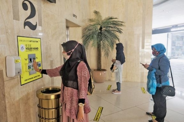 Pengunjung melambaikan tangan untuk membuka pintu lift yang telah dipasangi sensor nirsentuh di Mal Senayan City, Jakarta, kemarin.
