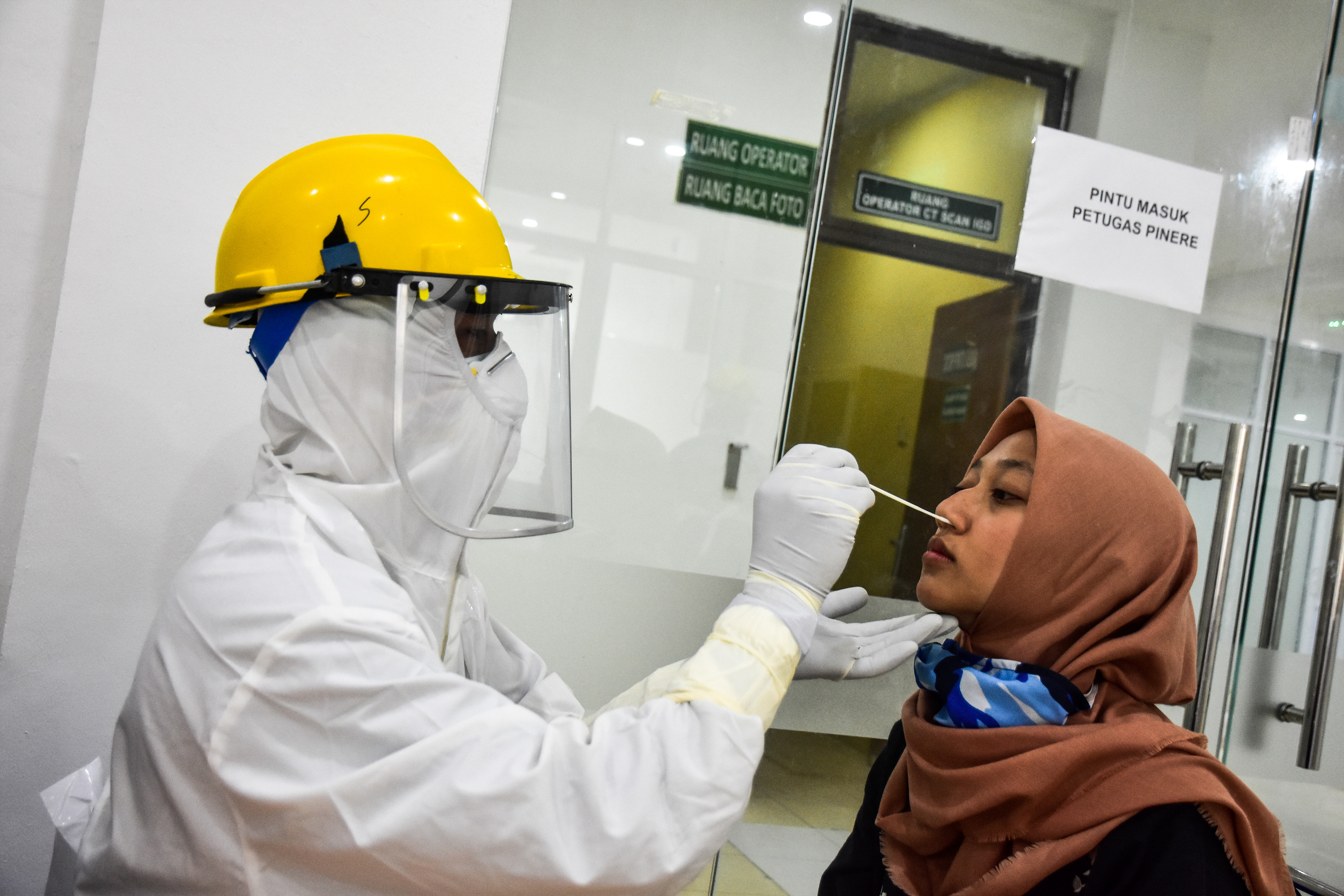  Tenaga kesehatan berpakaian pelindung diri mengambil spesimen lendir warga yang membayar untuk tes PCR