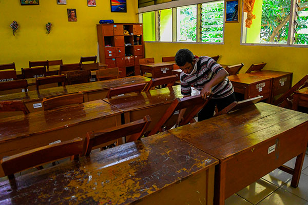 Petugas merapikan kursi diruang kelas 