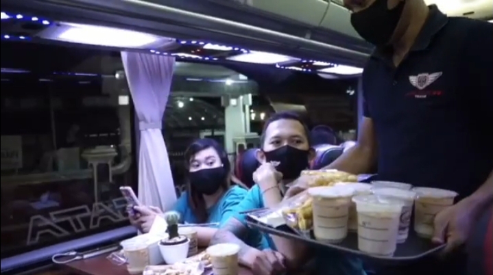 Seorang pramusaji tengah menawarkan kopi kepada penumpang bus wisata.