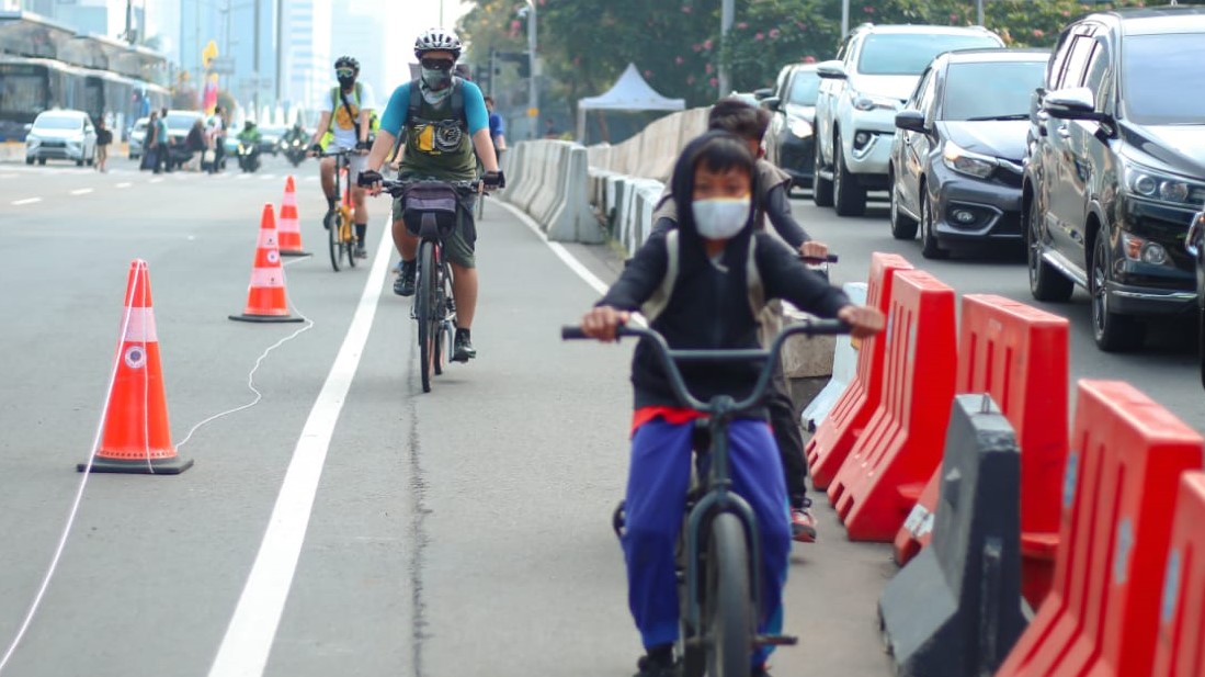 Para pesepeda melintasi jalur khusus di tengah keramaian lalu lintas.