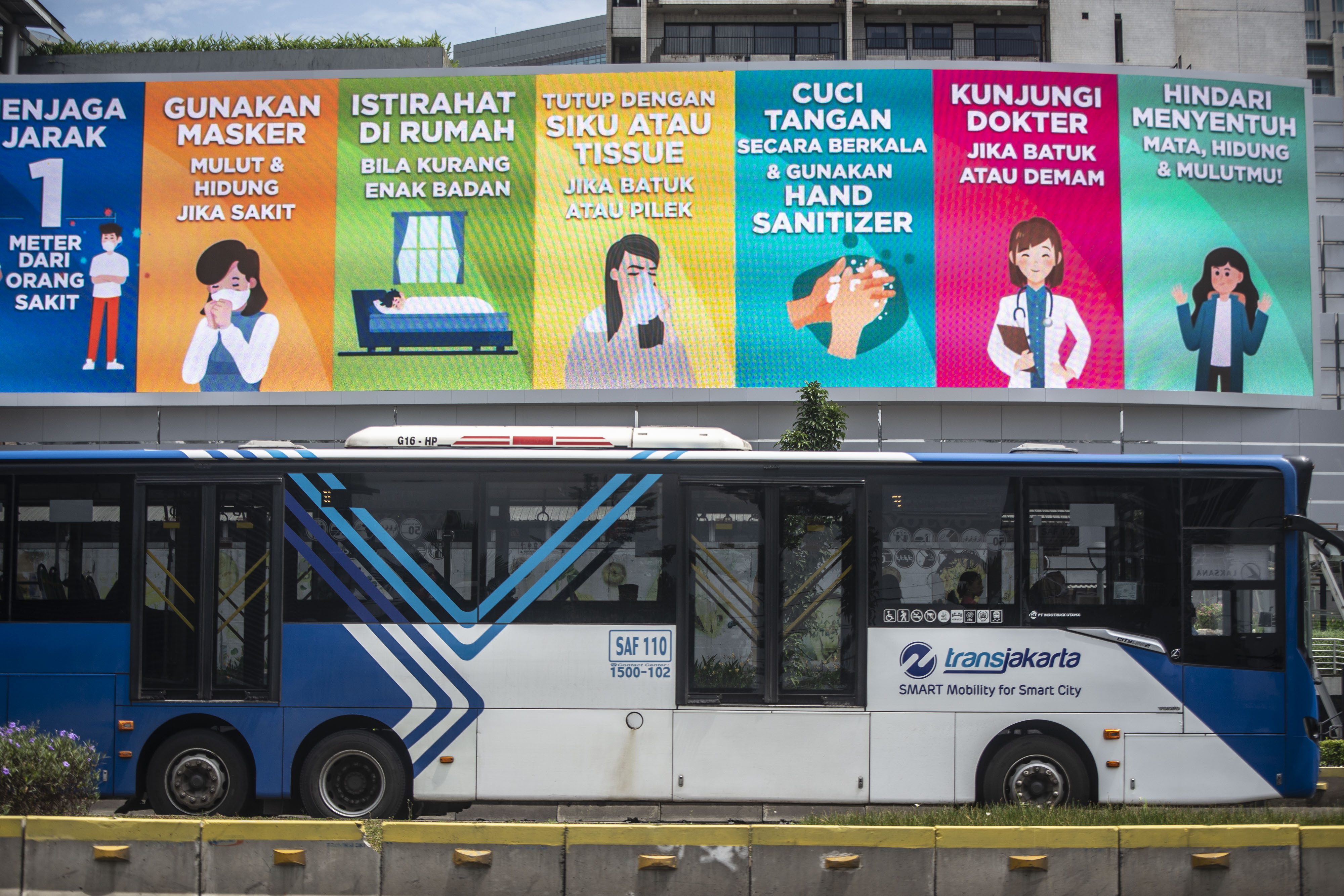 Bus TransJakarta melintasi papan iimbauan terkait pencegahan covid-19.
