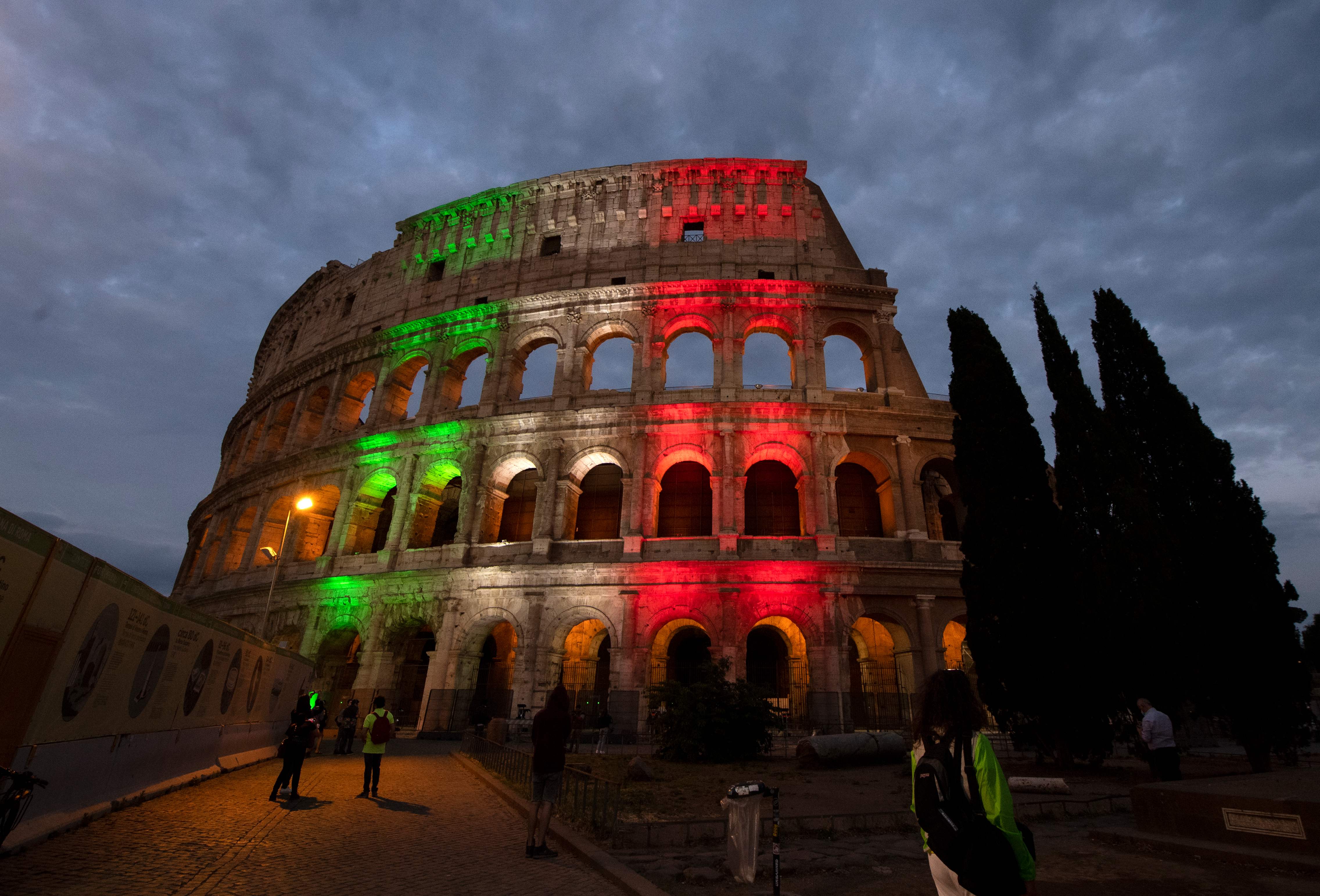  Warga sedang menikmati Colosseum yang dihiasi warna benderara Italia pada 31 Mei 2020