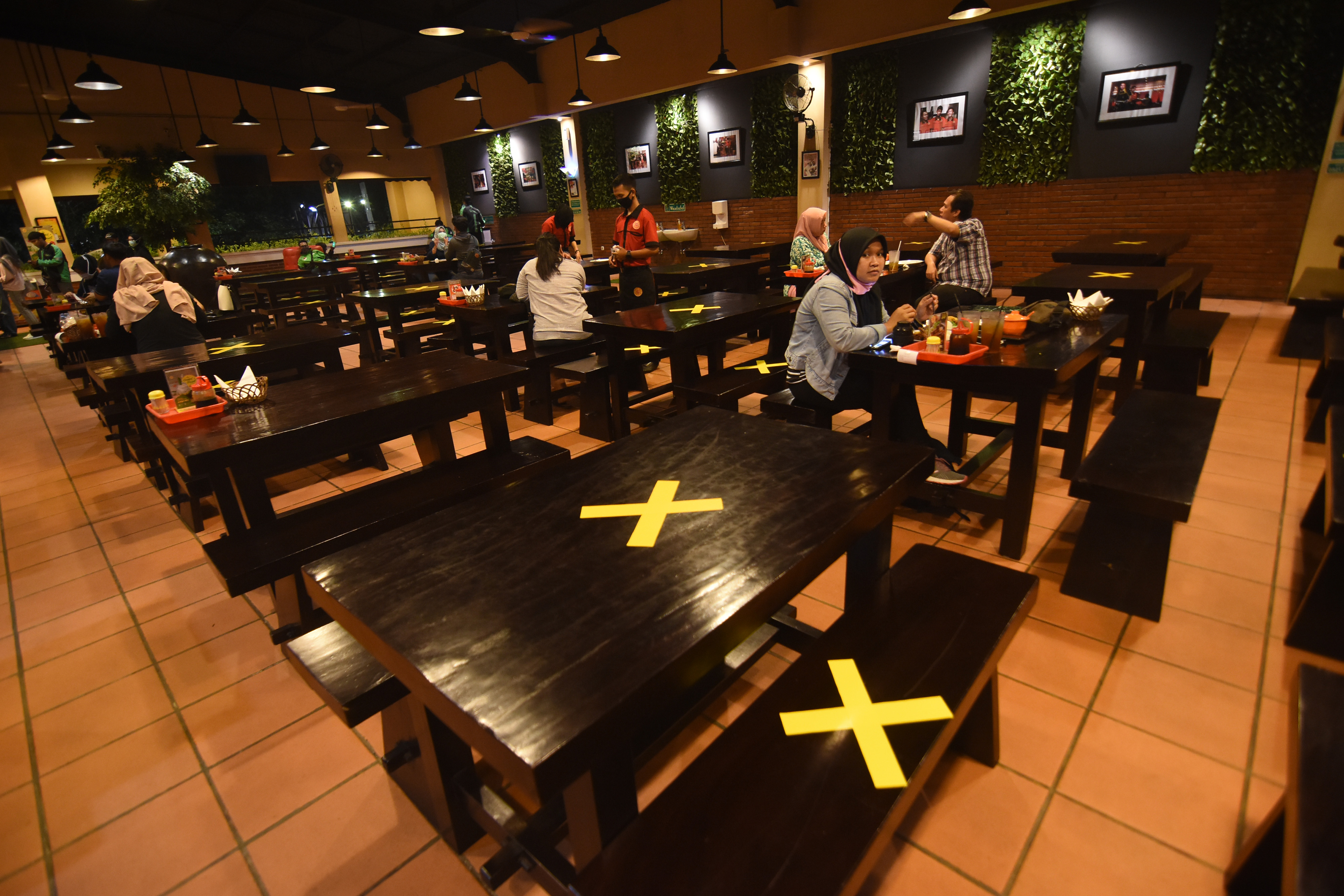 Pengunjung menyantap hidangan di antara meja yang diberi tanda silang di restoran di Srengseng Sawah, Jakarta Selatan