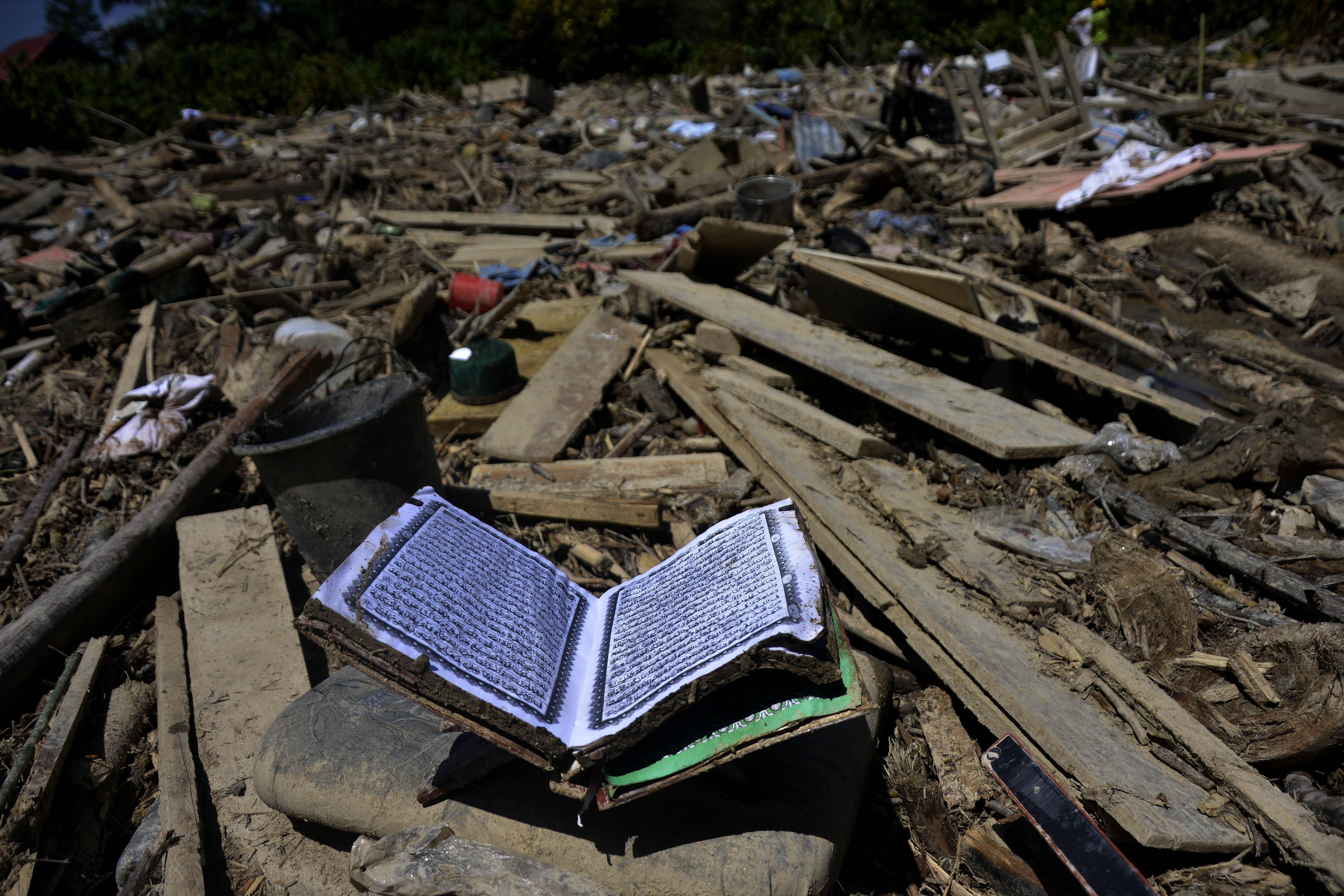 Sebuah Al Quran di antara tumpukan material lumpur dan kayu pascabanjir bandang di Desa Radda, Luwu Utara.
