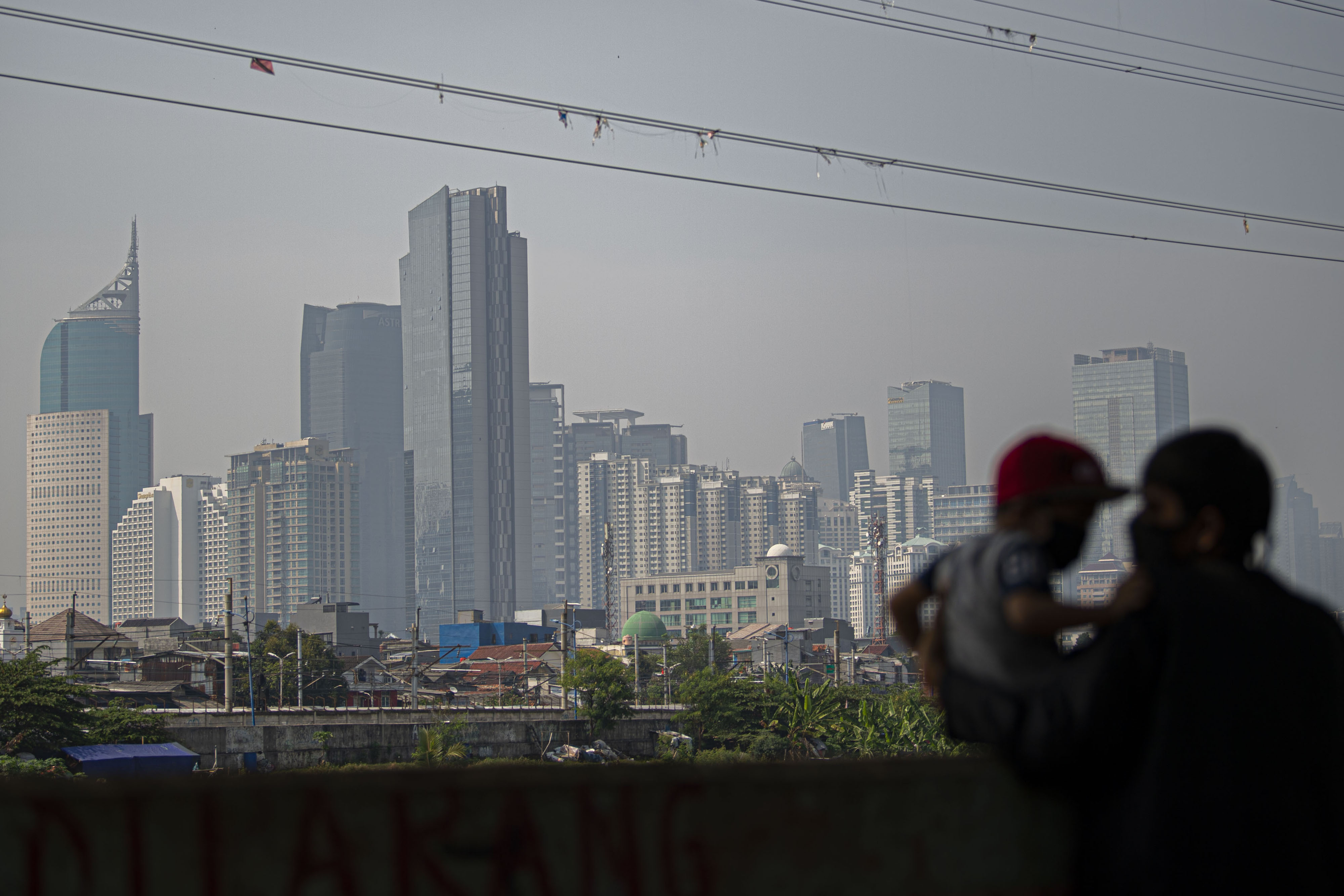 Warga bermain bersama anaknya dengan latar belakang gedung pencakar langit di Jakarta.