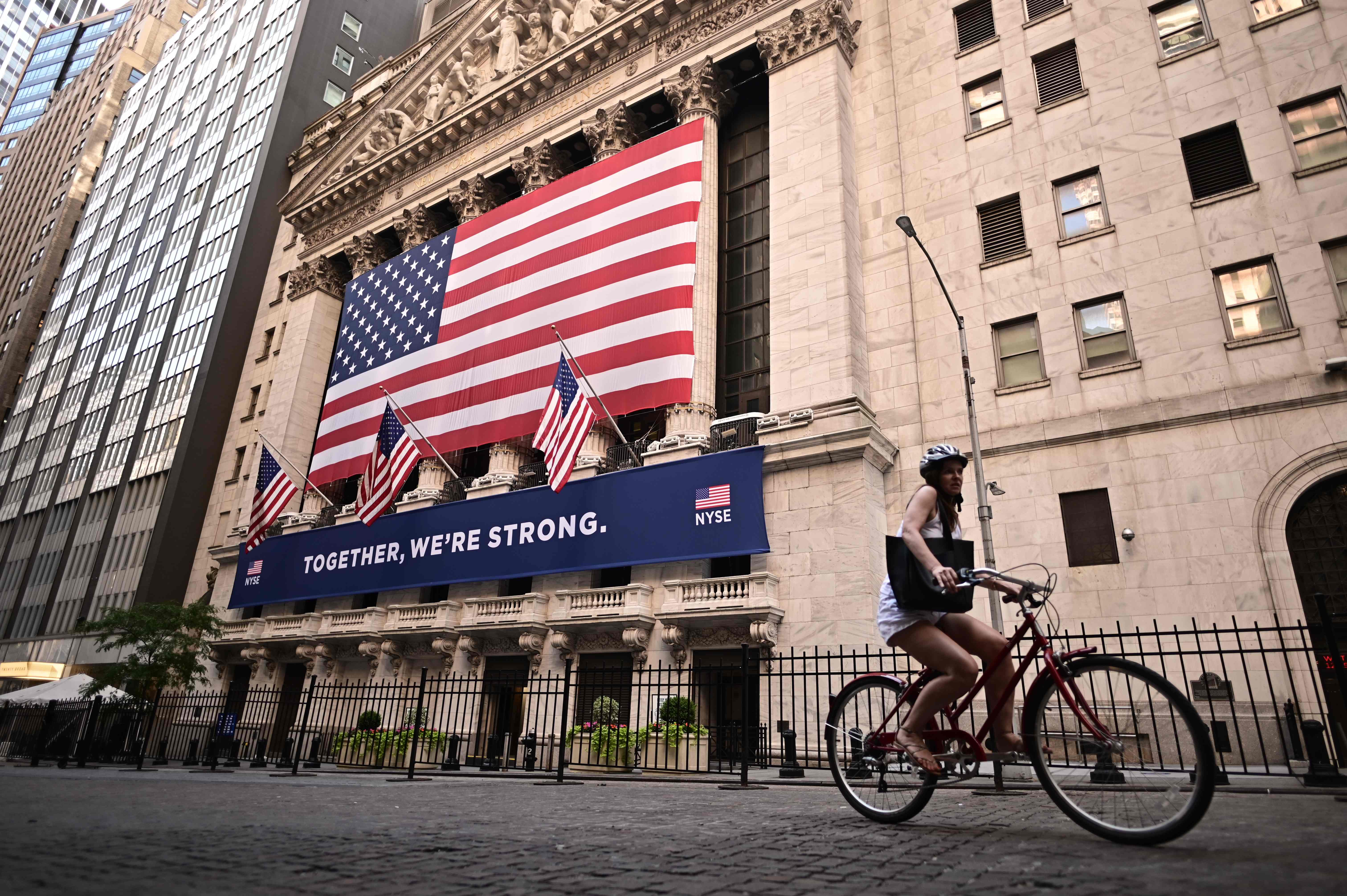 Pesepeda melintas di depan gedung bursa saham New York Wall Street. Saham-saham AS rontok setelah jutaan korban PHK ajukan tunjangan.