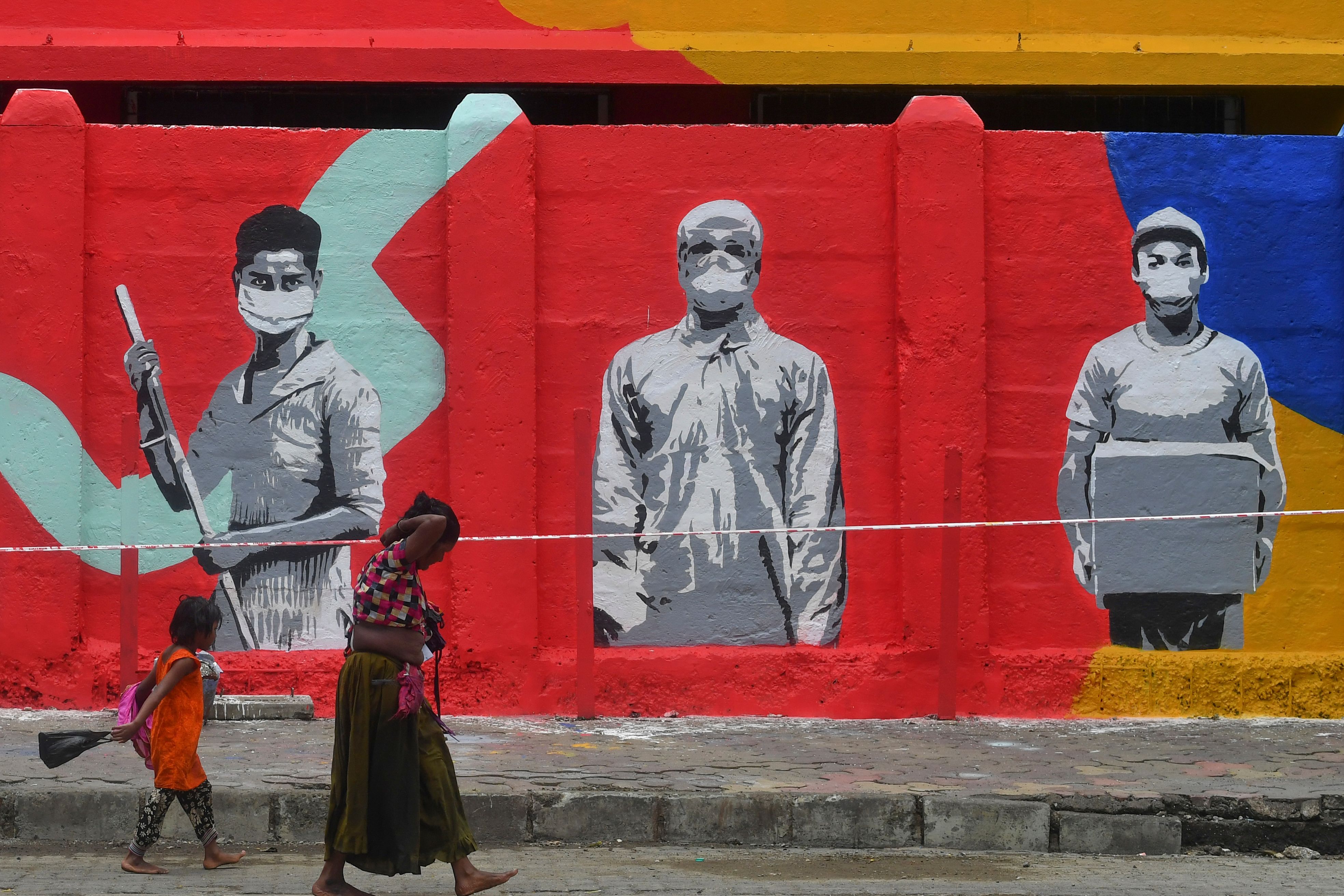 Seorang ibu dan anaknya berjalan melintasi mural terkait pandemi covid-19 di wilayah Mumbai, India.