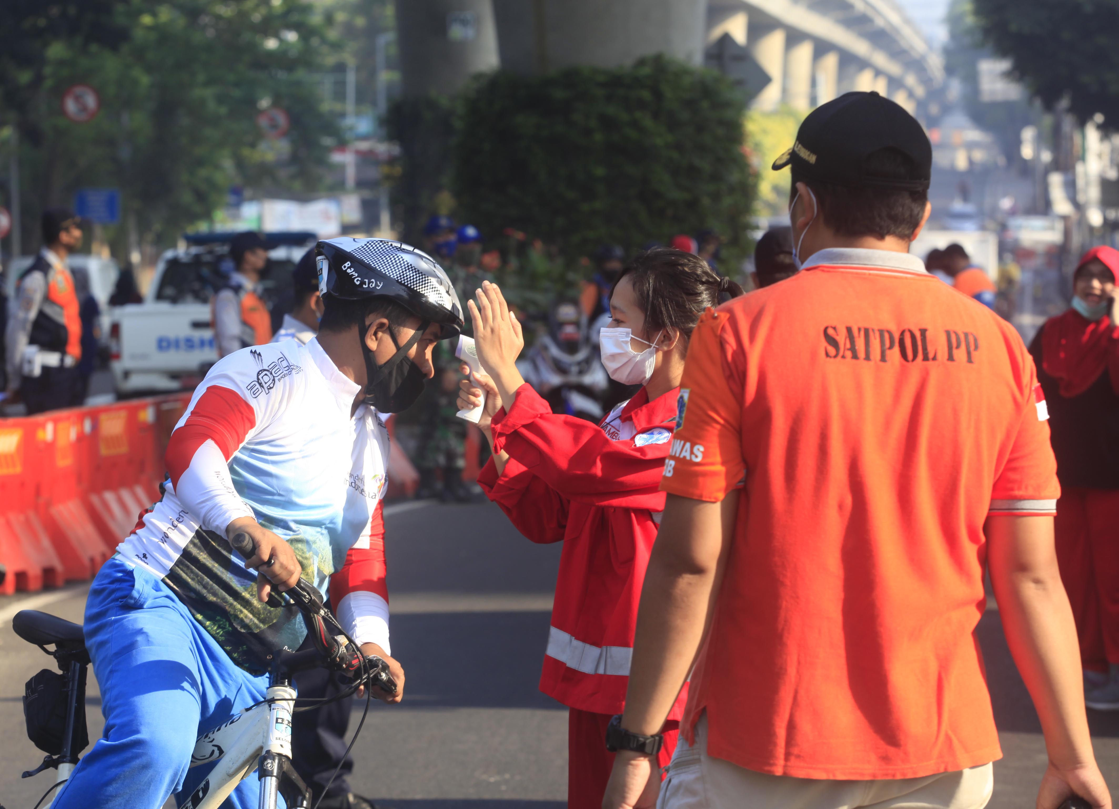 Petugas Satpol PP dan Petugas Kesehatan mengecek suhu masyarakat yang akan masuk wilayah HBKB di Jalan Layang Non Tol, Pangeran Antasari.