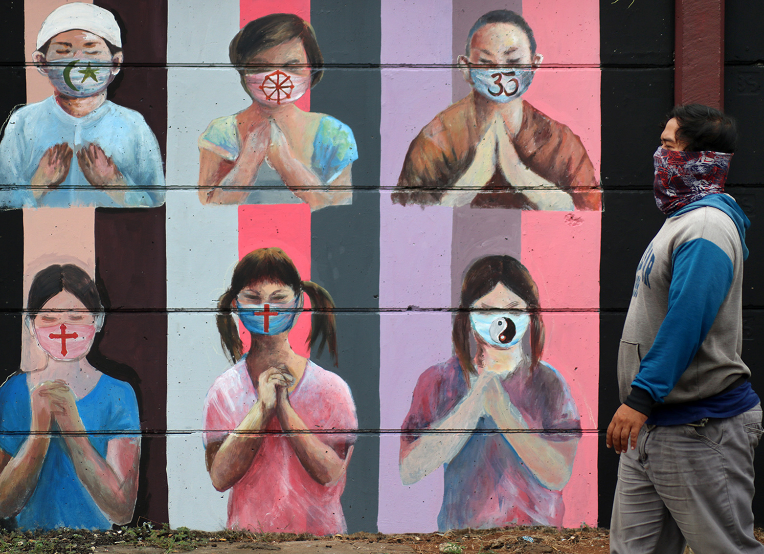 Warga melintas di dekat mural penggunaan masker yang mewakili umat beragama di Jalan Juanda, Depok