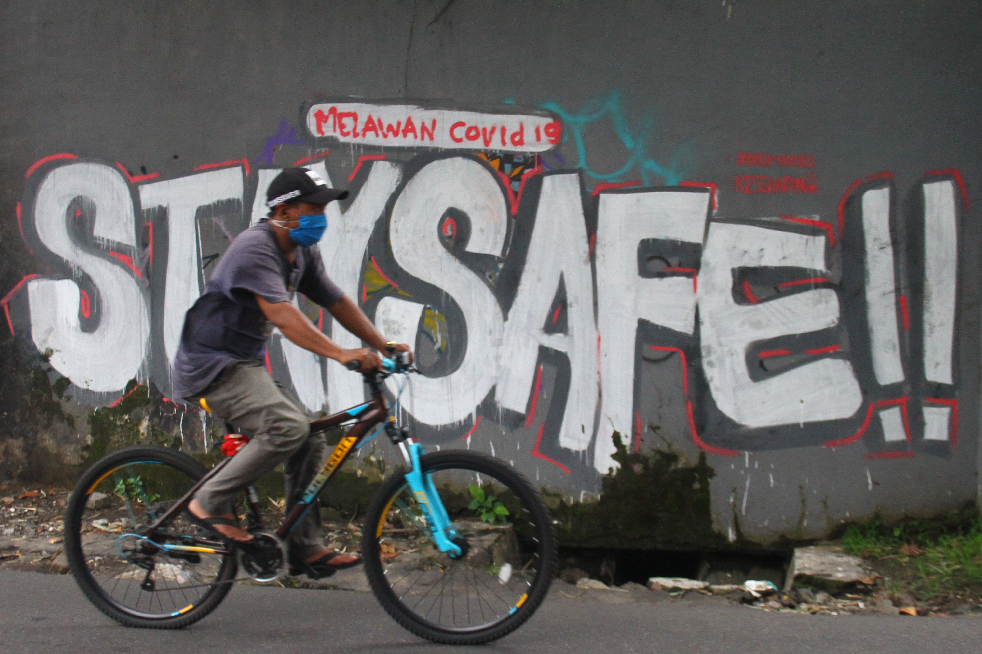 Pesepeda melintasi mural kampanye covid-19 di Malang, Jawa Timur.