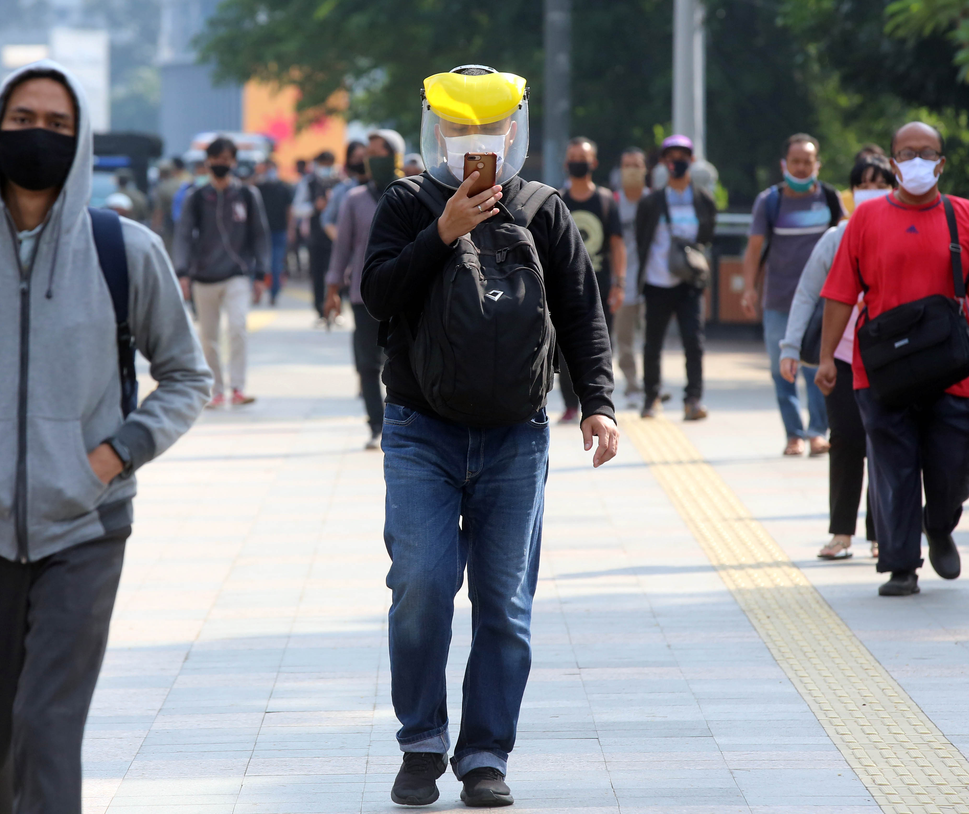 Pekerja menggunakan masker dan pelindung wajah menuju kantornya saat melewati trotoar di kawasan Sudirman