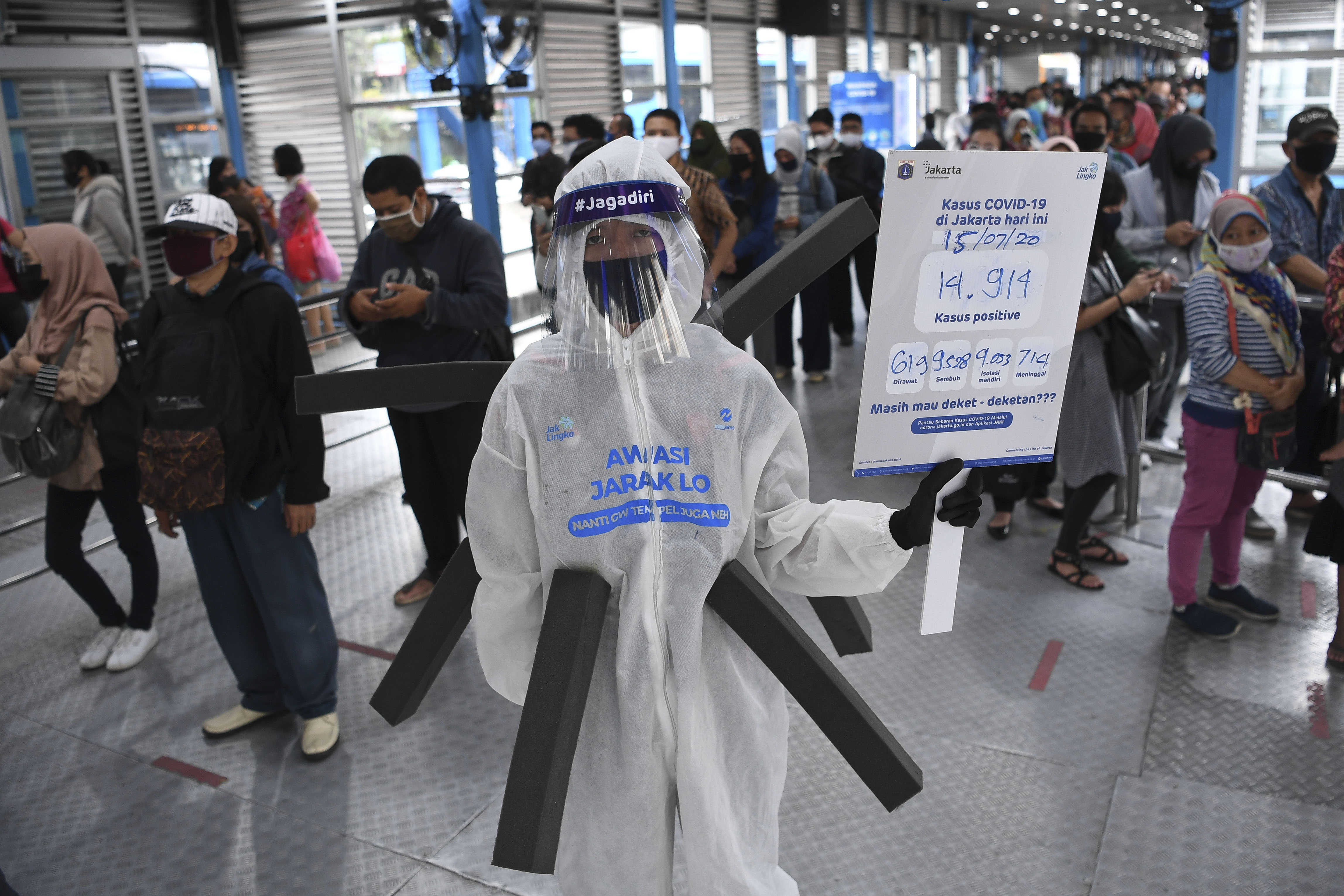 Komunitas pecinta Transjakarta mengenakan baju hazmat dengan membawa poster informasi covid-19.