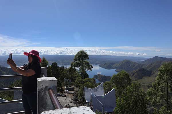 Seorang wisatawan berswafoto di menara pandang tele, kabupaten samosir berlatar belakang Kaldera Danau Toba