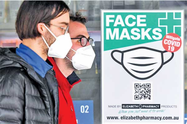 Pejalan kaki mengenakan masker saat melintas di depan kampanye di Melbourne, Australia