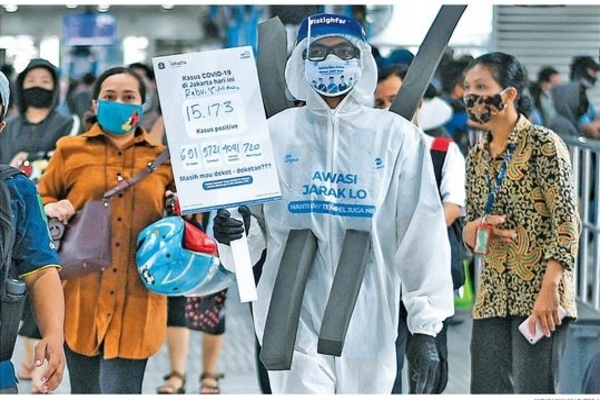 Anggota komunitas pecinta Trans-Jakarta berbaju hazmat membawa poster berisi informasi covid-19 di Halte Harmoni, Jakarta, kemarin.