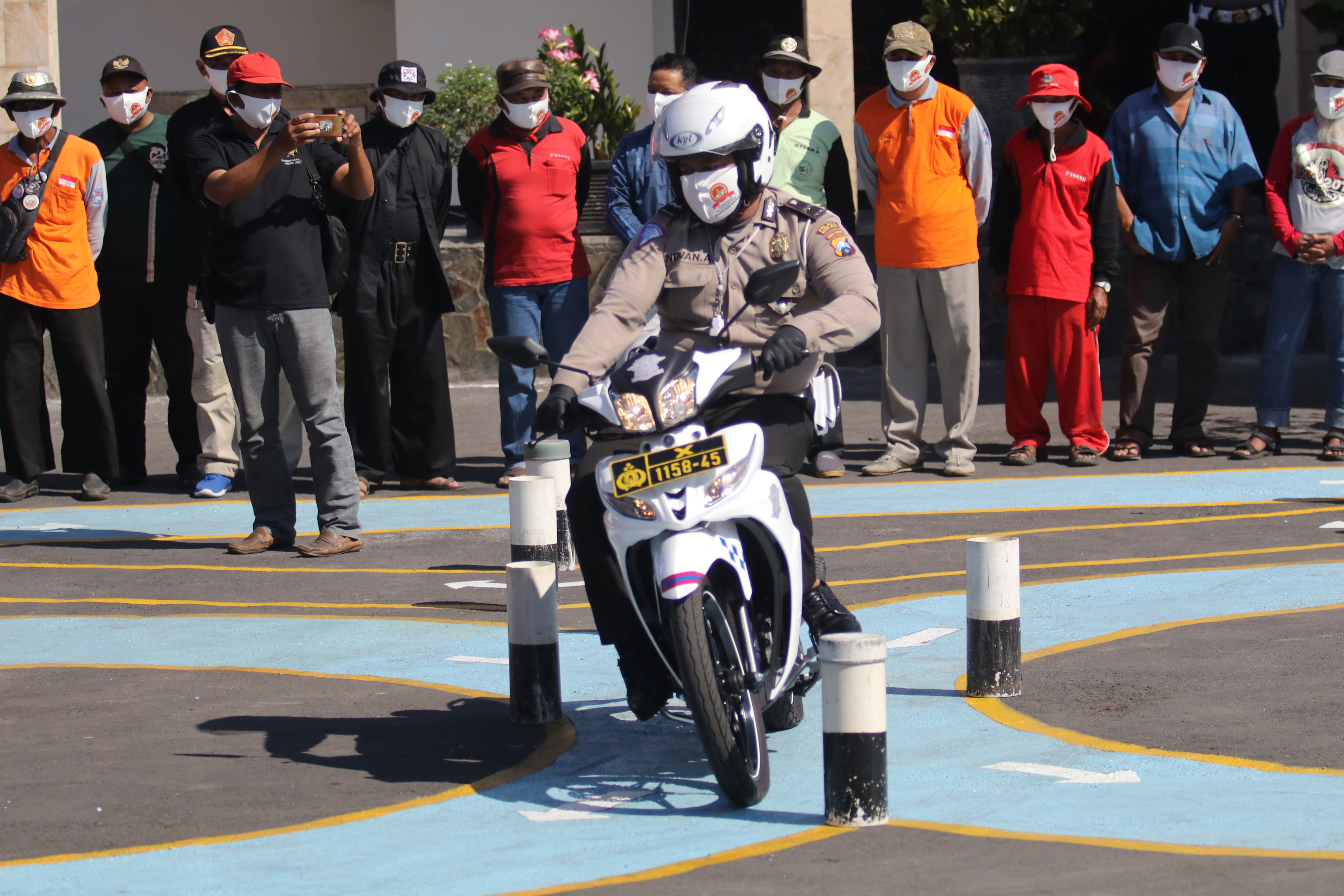 Anggota polisi memberi contoh berkendara aman dengan menerapkan protokol kesehatan di hadapan ojek dan warga.