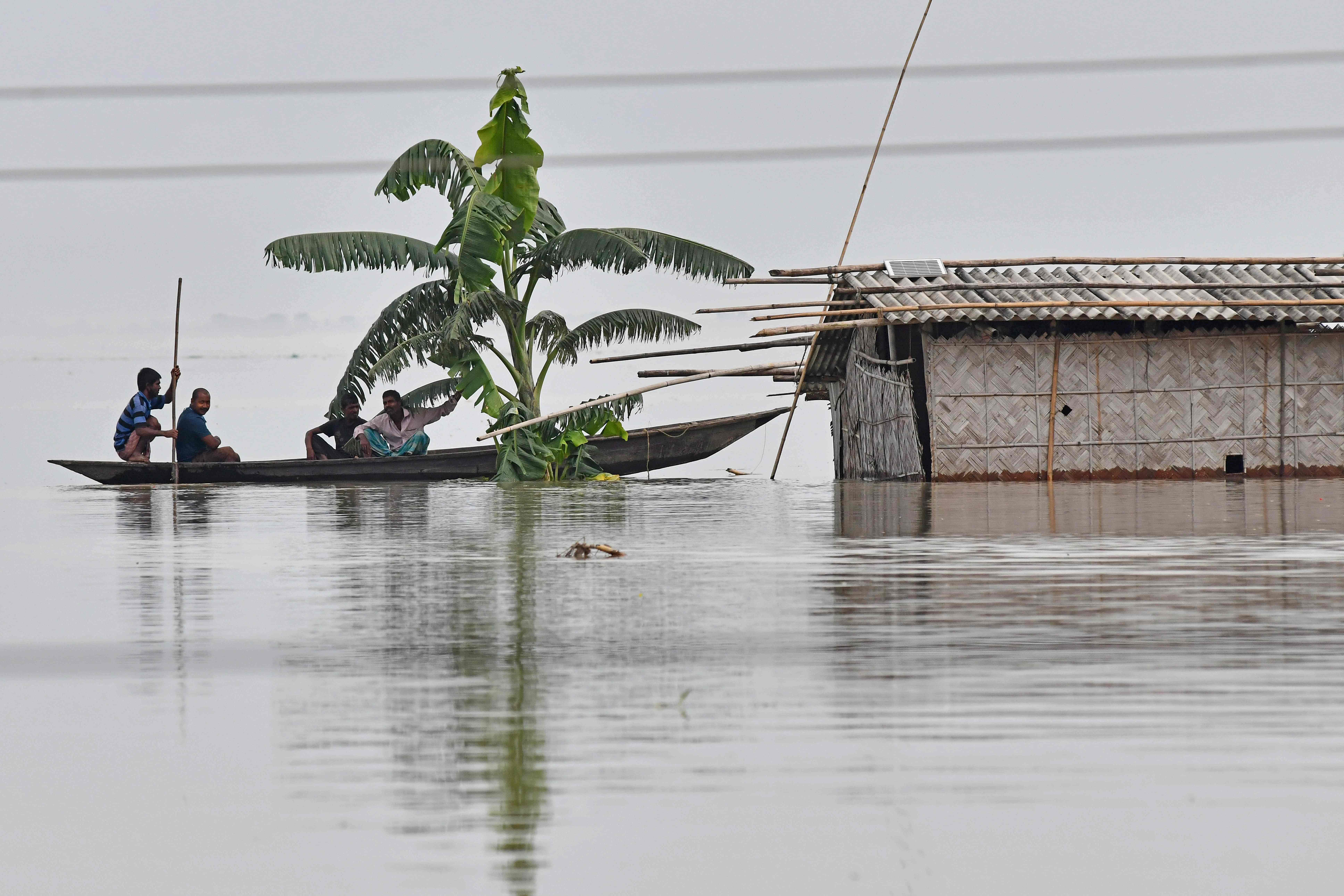 Warga desa mengayuh perahu mendekati sebuah rumah yang terendam di Distrik Kamrup, Negara Bagian Assam, India, Selasa (14/7).  