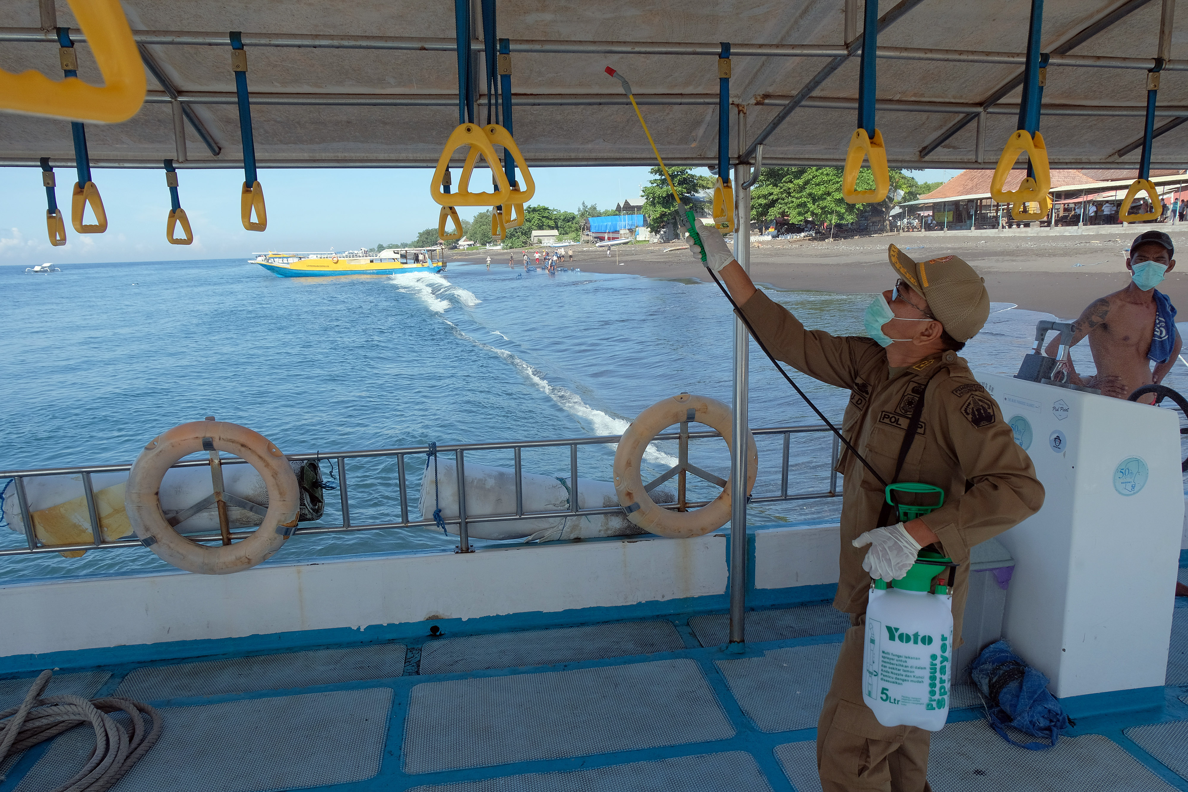Anggota Satpol PP Provinsi Bali menyemprotkan cairan disinfektan pada bagian pegangan tangan di kapal cepat di Pelabuhan Tribuana, Klungkung