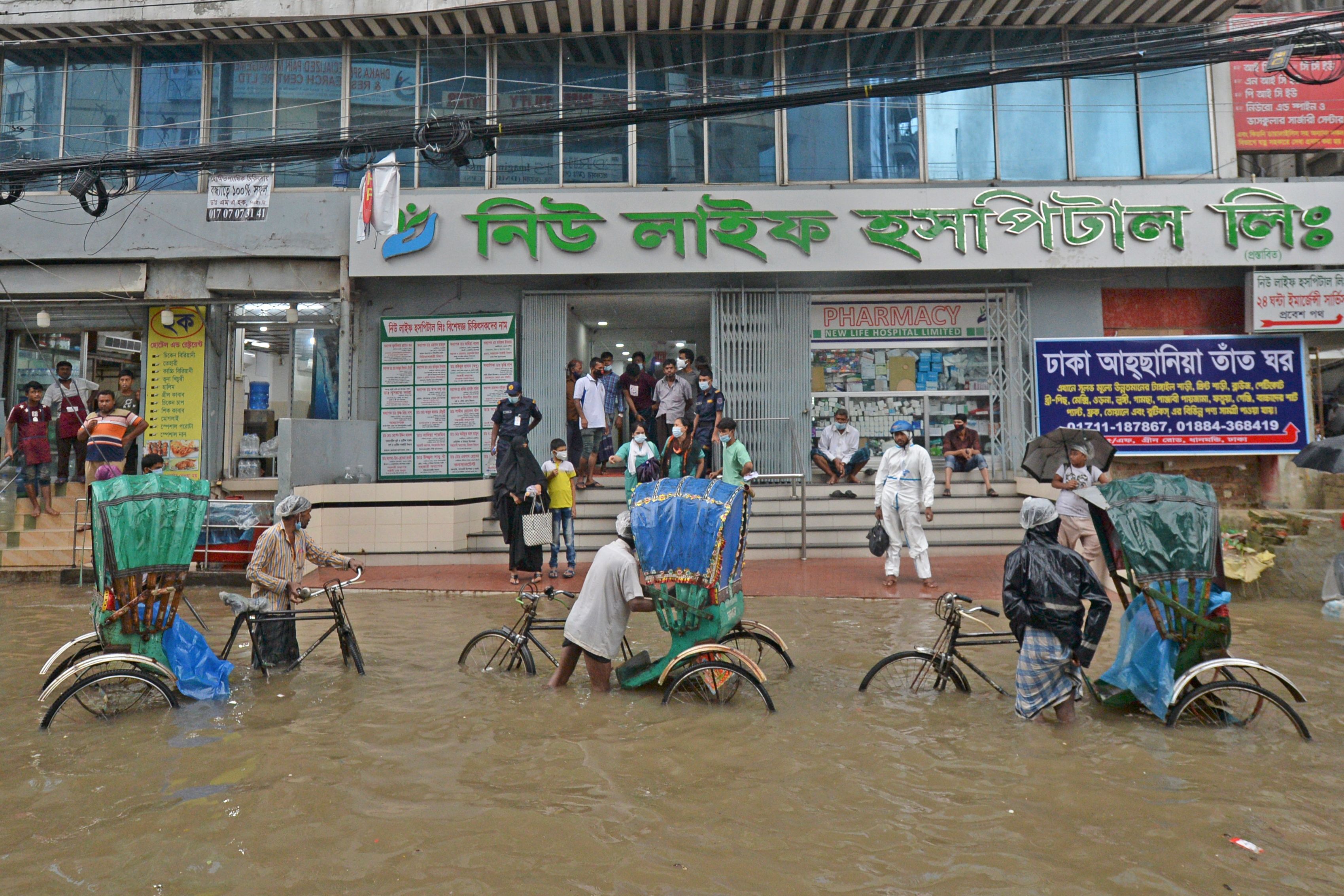 Para pengemudi angkong (rickshaw) bertahan di tengah banjir menunggu para penumpang di depan toko di Kota Dhaka, Bangladesh, 21 Juli 2020.