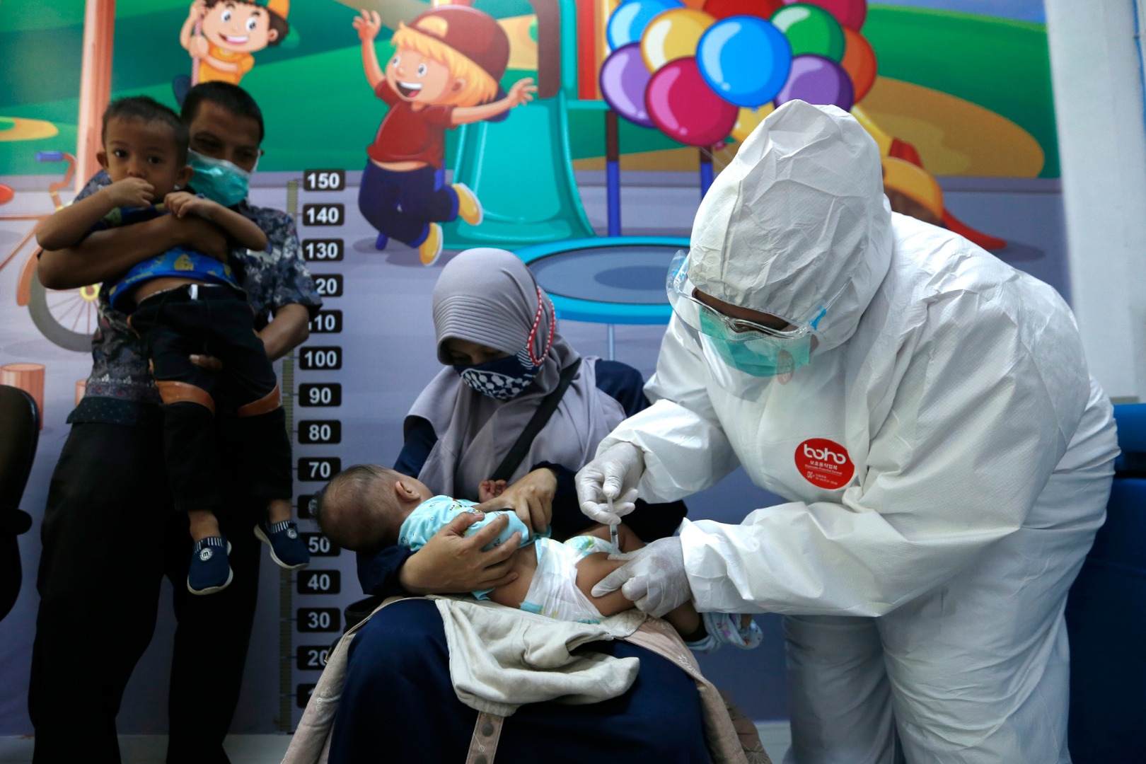 Petugas medis puskesmas Ulee Kareng memakai APD saat memberikan imunisasi kepada anak balita di Banda Aceh, Aceh, Kamis (16/7).