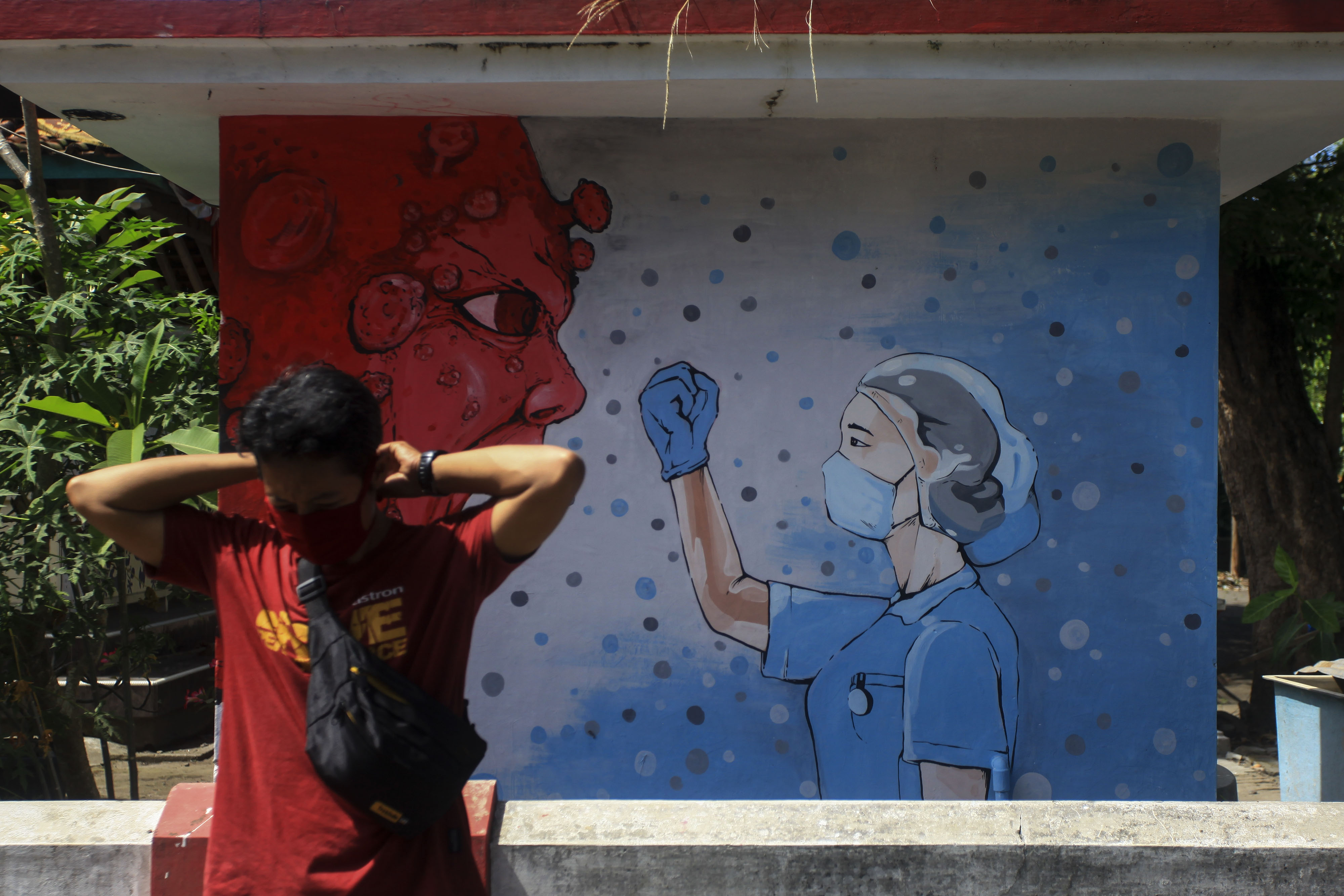 Warga berada di dekat mural bergambar tenaga medis dan virus corona