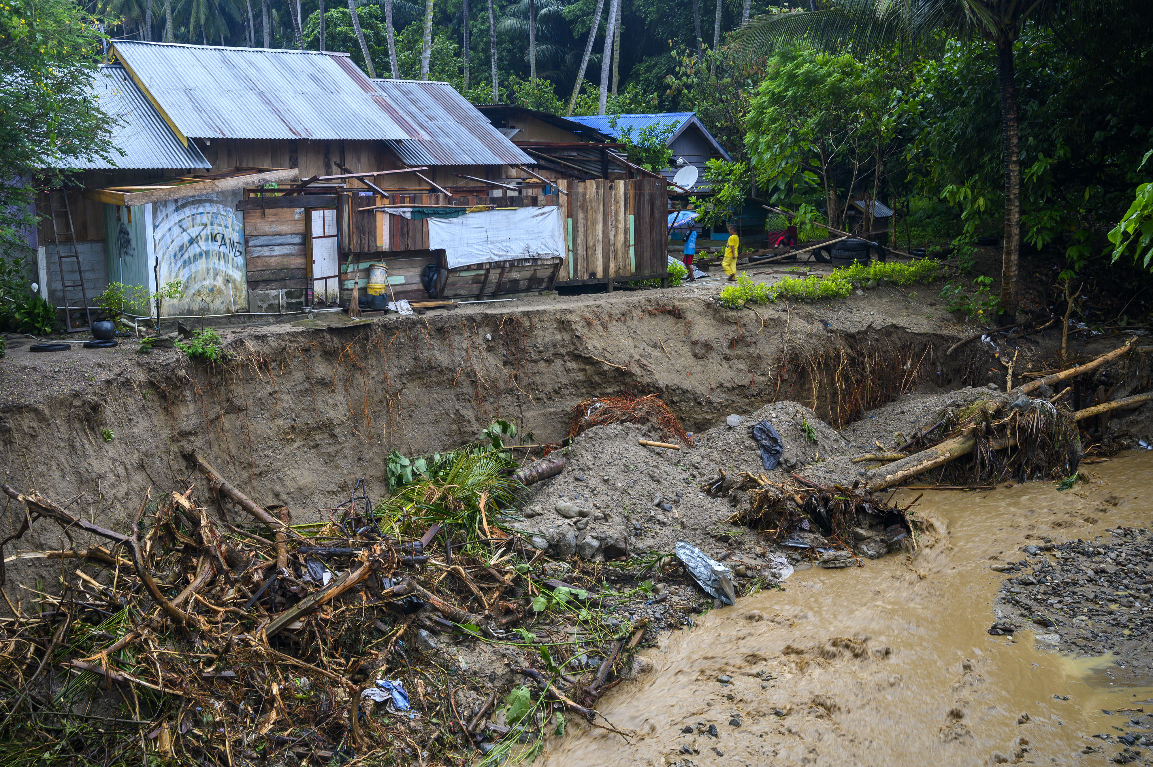 Warga berada di dekat rumah yang terancam ambruk akibat abrasi sungai di Desa Simoro, Kabupaten Sigi, Sulawesi Tengah, Senin (6/7/2020).