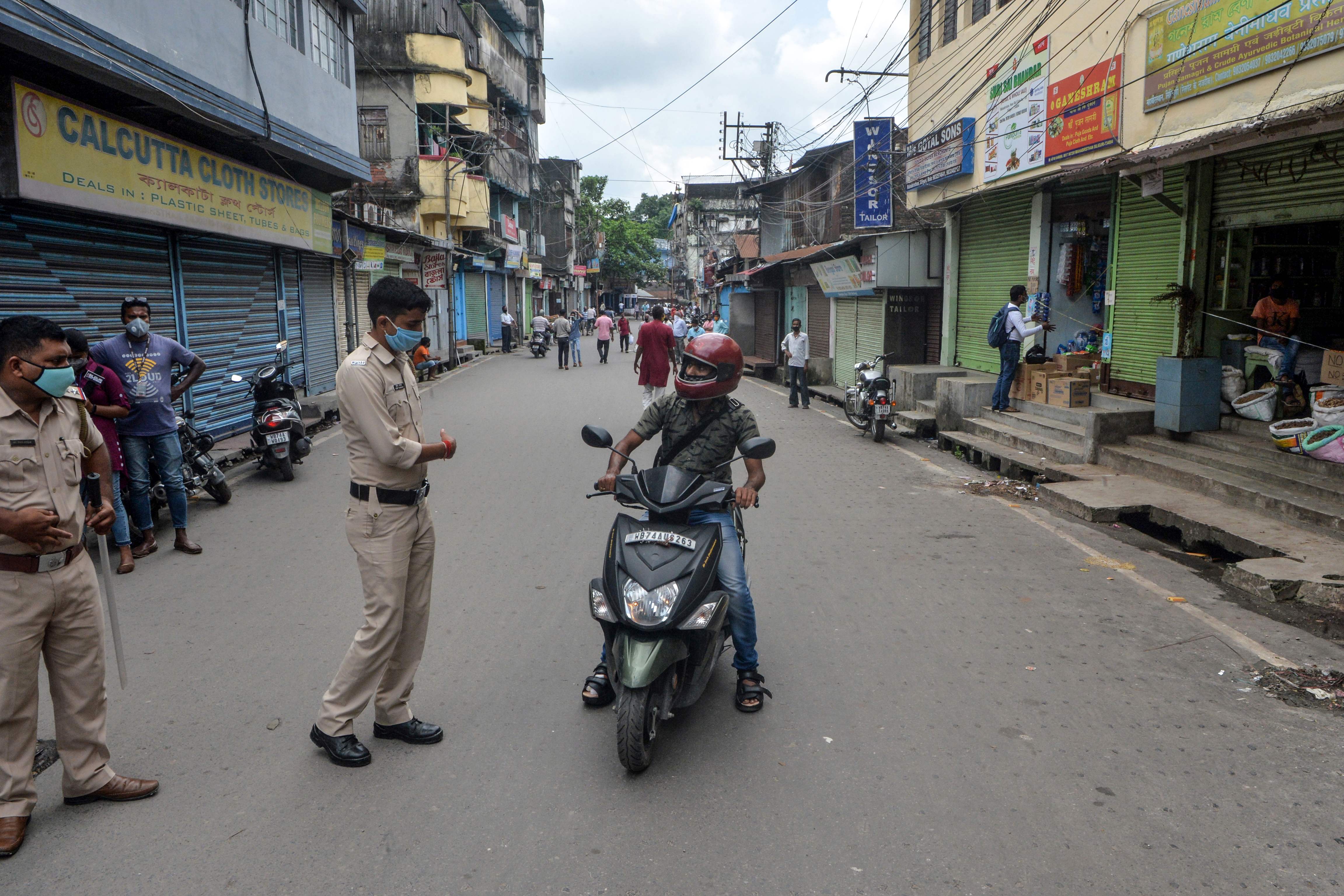 Polisi menghentikan pengendara sepeda motor yang hendak masuk pasar yang ditutup karena lockdown lagi di Siliguri, India, Kamsi (16/7).