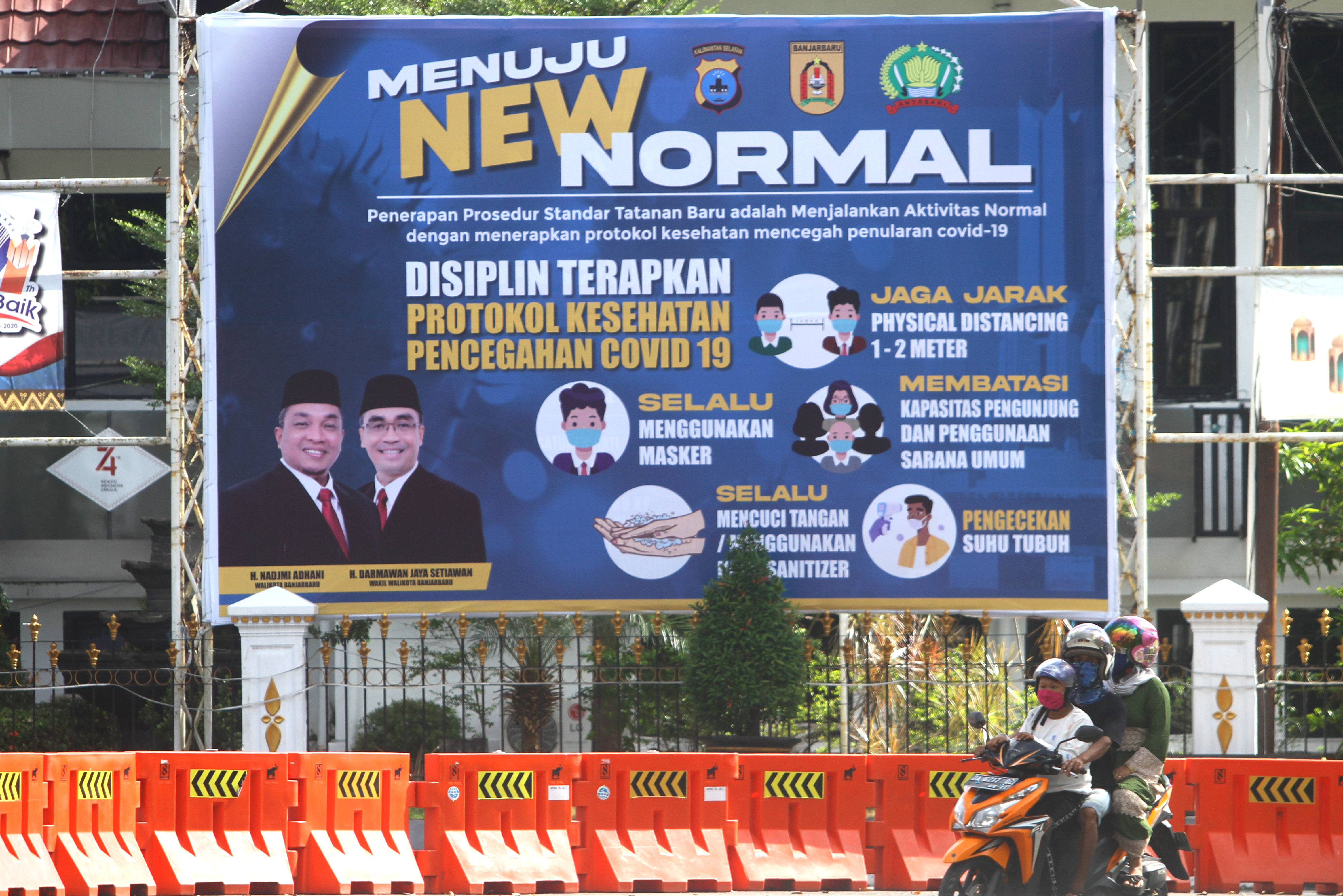 Pengendara motor melintas di dekat spanduk protokol kesehatan COVID-19 di Jalan Panglima Batur, Banjarbaru, Kalimantan Selatan.