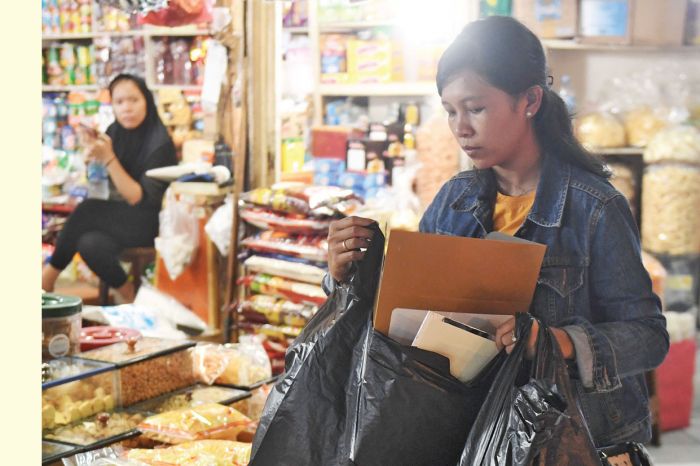 Seorang perempuan membawa barang belanjaan di sebuah pasar.  