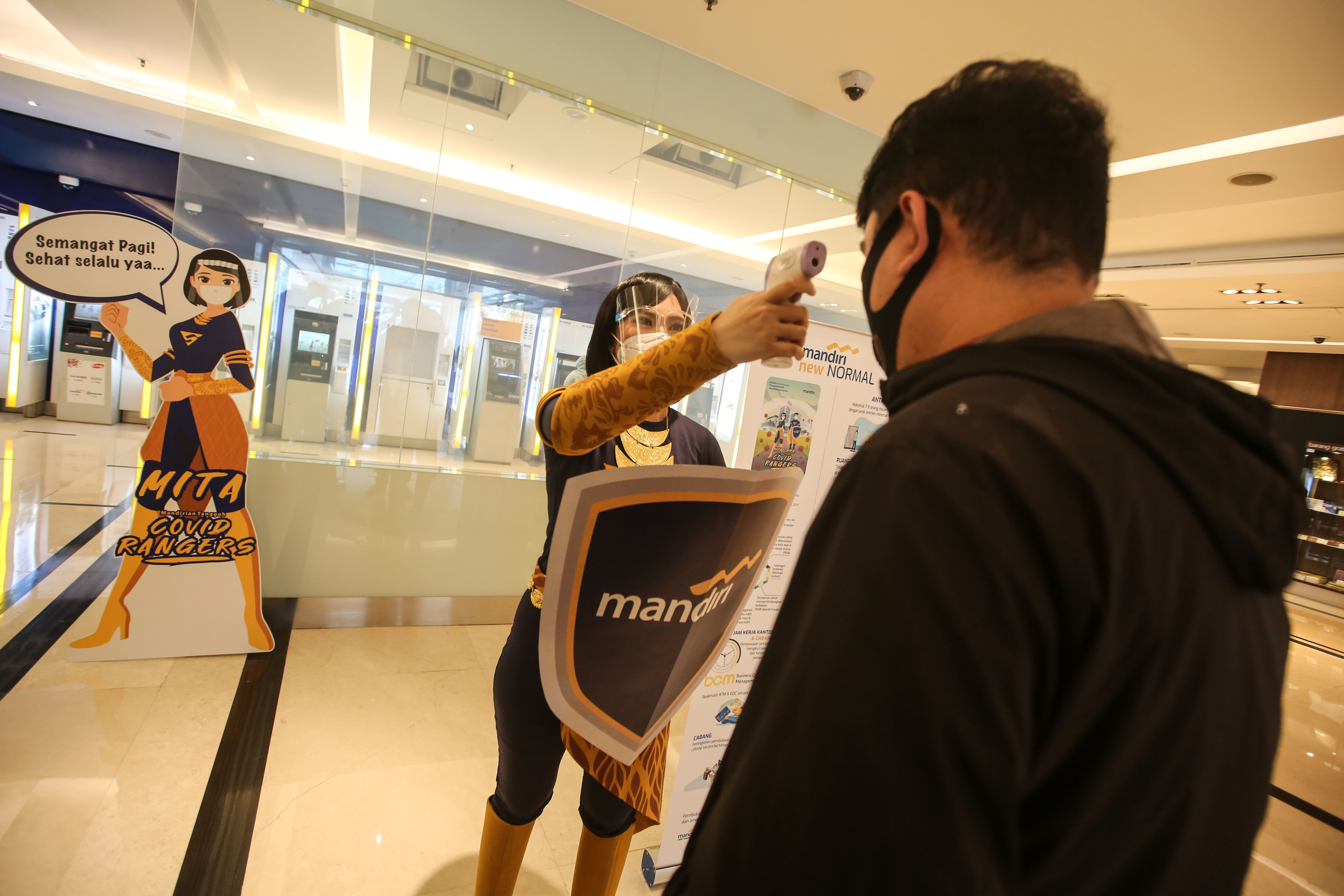 Maskot Mandiri Covid Rangers Dika dan Mita melakukan pengecekan suhu tubuh kepada pengunjung di lingkungan Bank Mandiri, Jakarta.