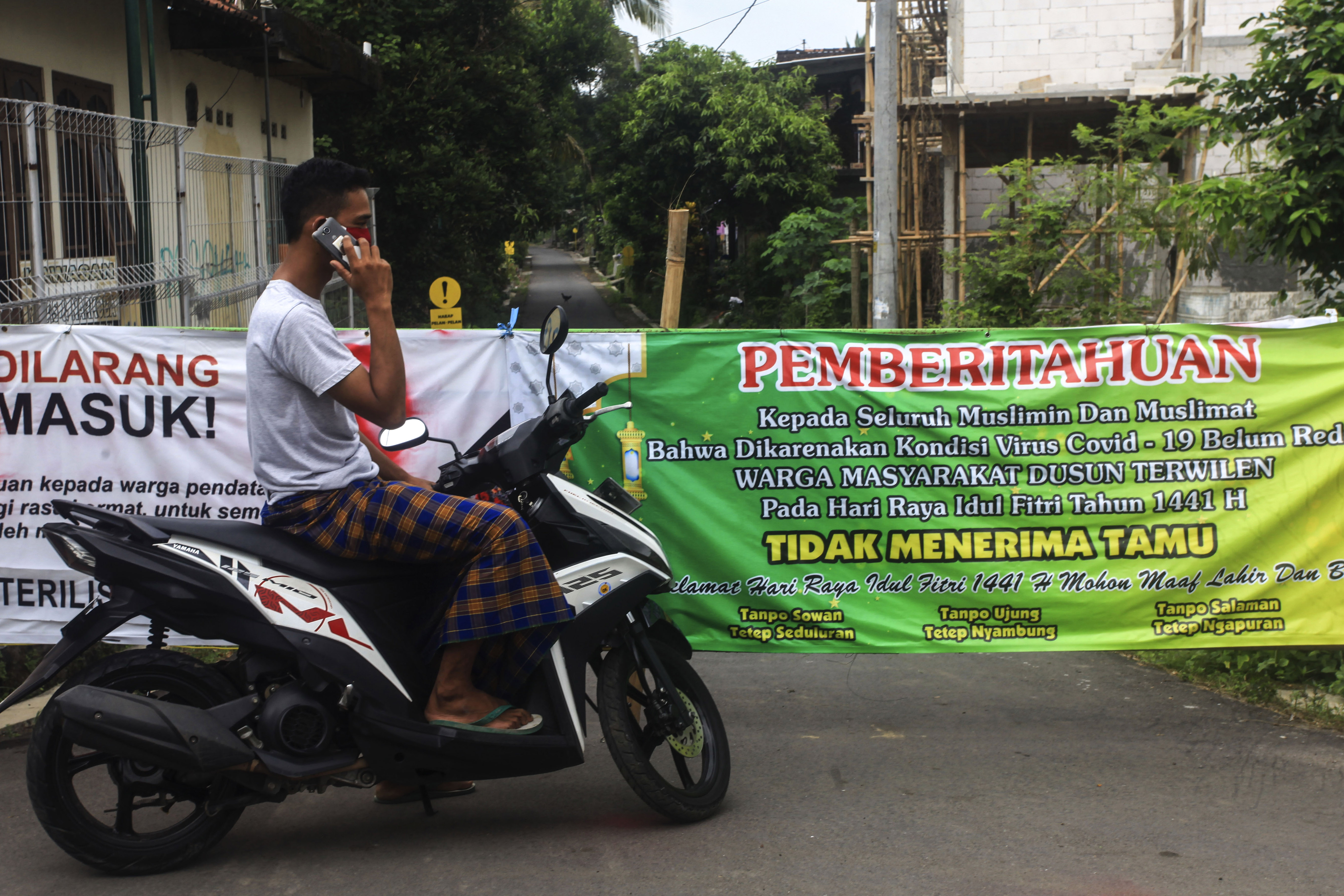 Warga berada di pintu masuk kampung yang ditutup di Terwilen, Margodadi, Seyegan, Sleman, Daerah Istimewa Yogyakarta (DIY), Selasa (26/5).