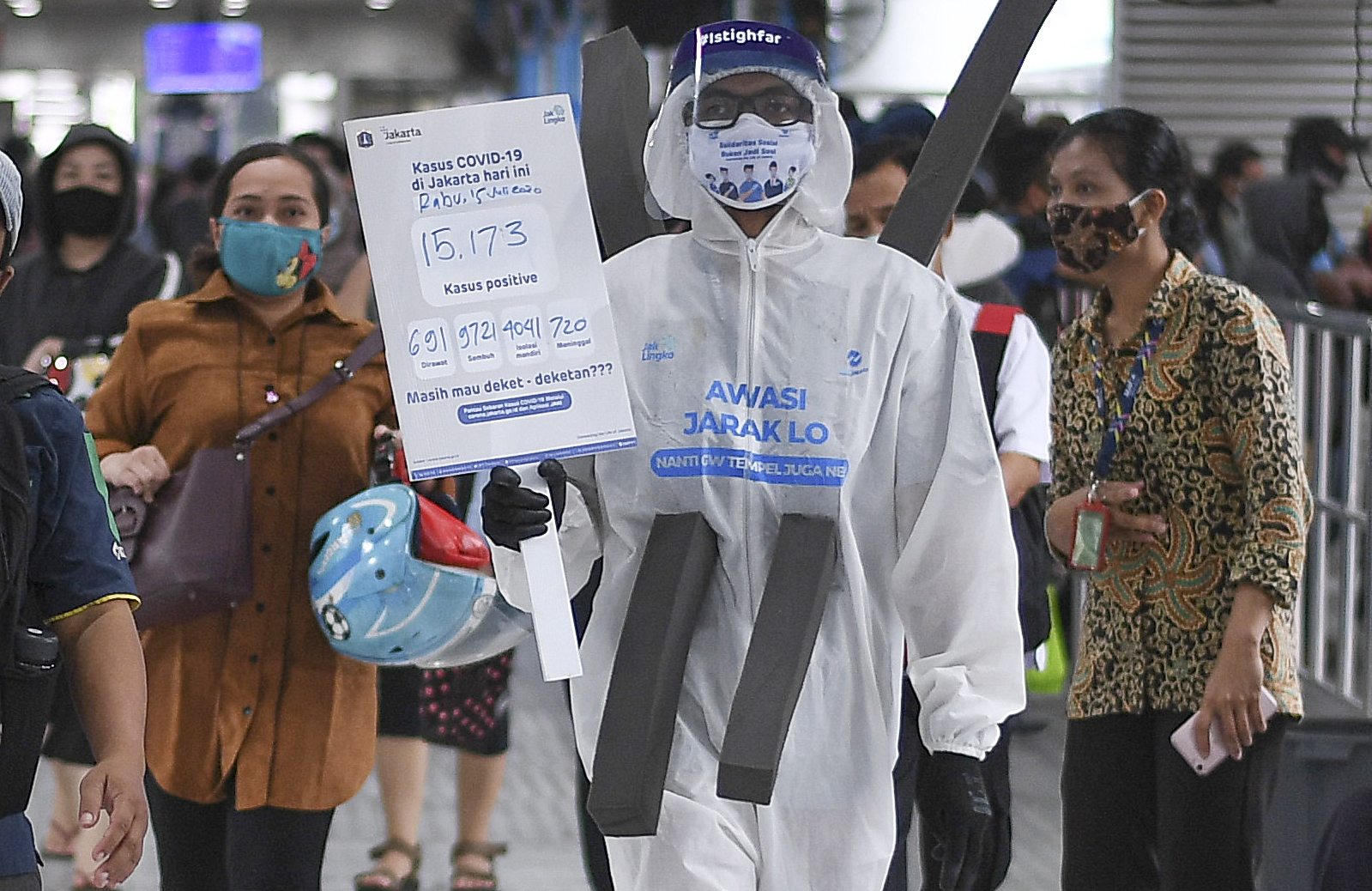 Anggota komunitas pecinta Transjakarta mengenakan baju hazmat melakukan sosialisasi protokol kesehatan di Halte Transjakarta Harmoni