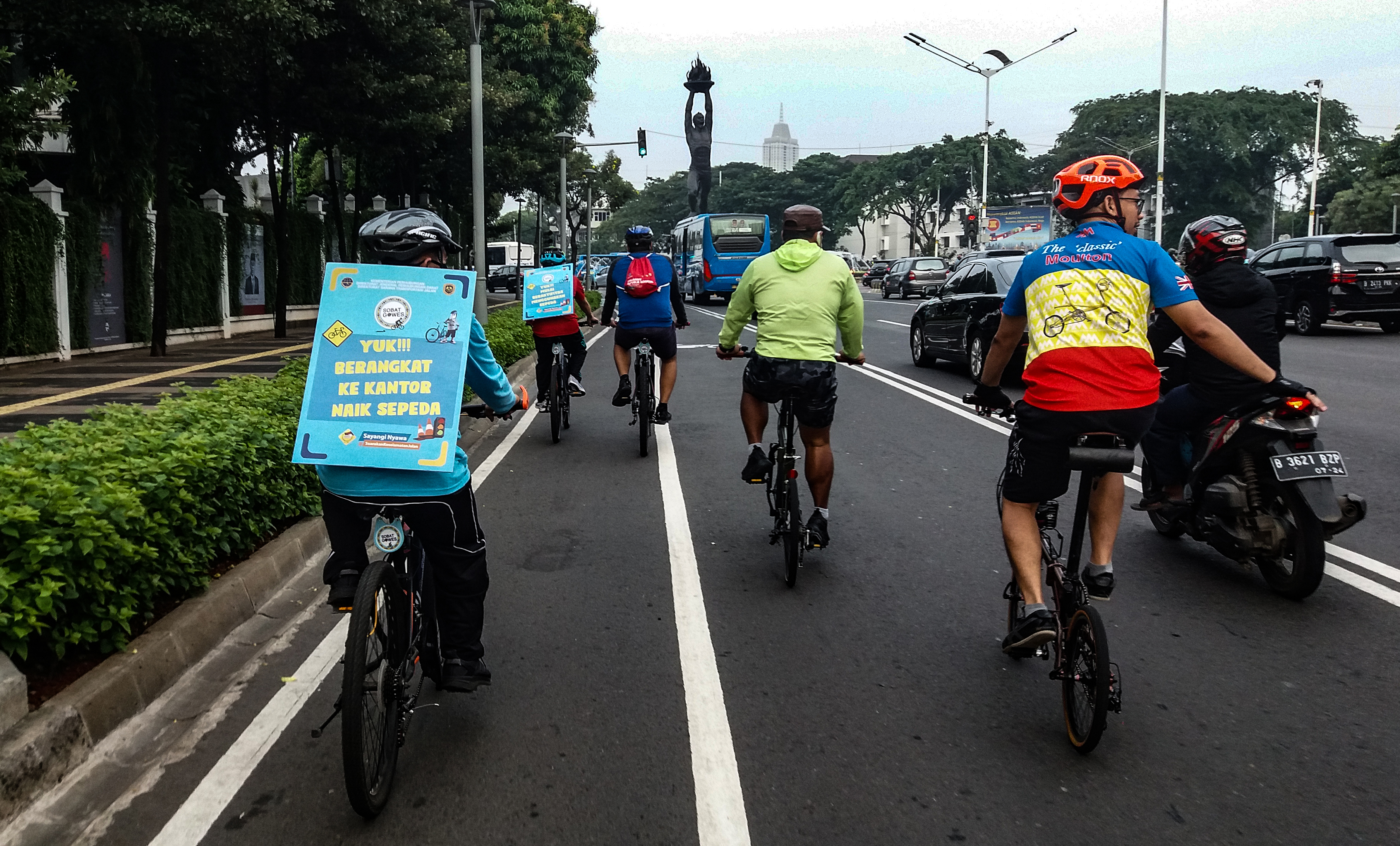 Pekerja menggunakan sepeda dan membawa poster imbauan mengajak bersepeda menuju kantor