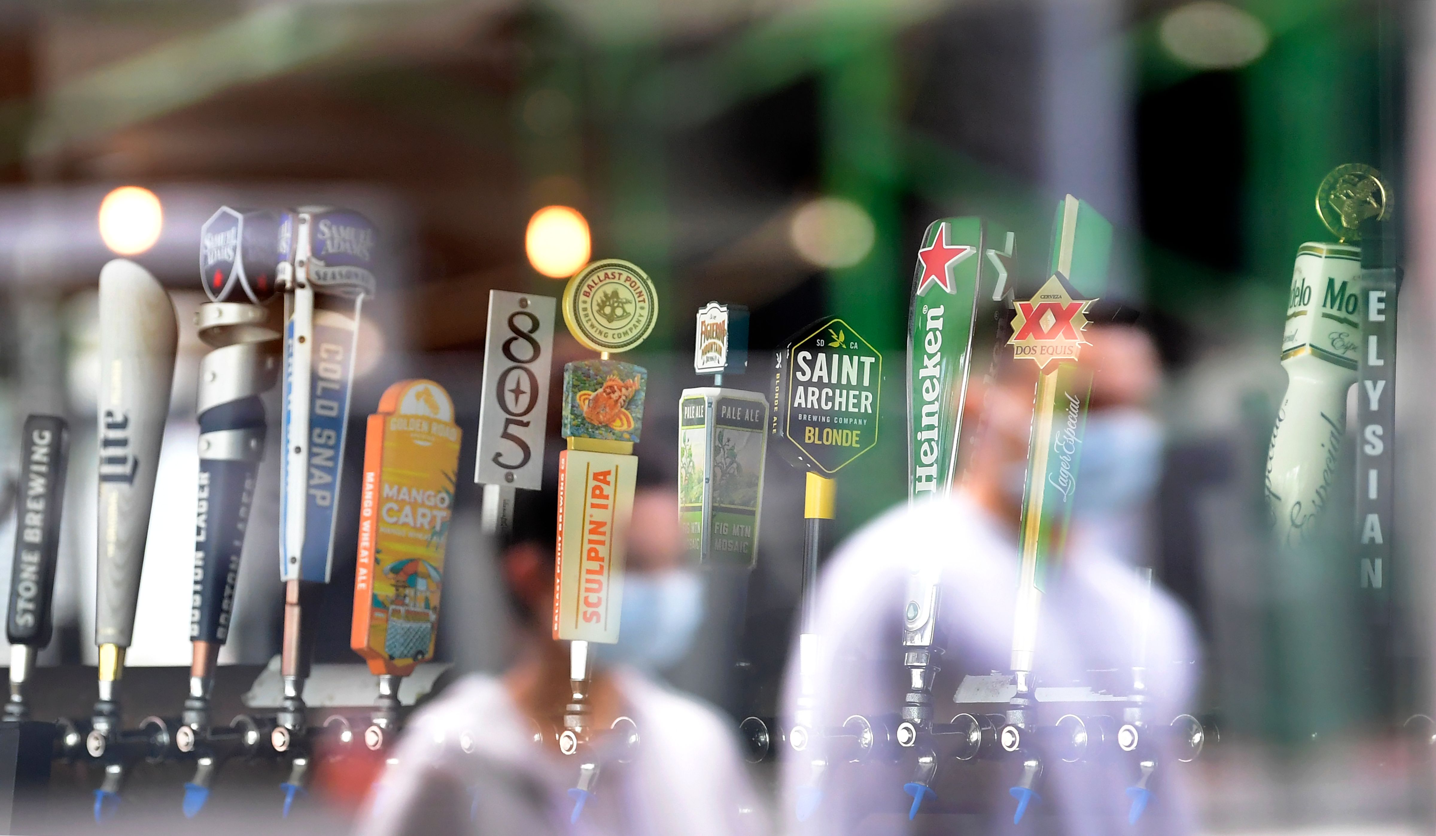 Refleksi pejalan kaki yang mengenakan masker wajah terlihat saat mereka melewati  bar di Los Angeles pada 29 Juni 2020