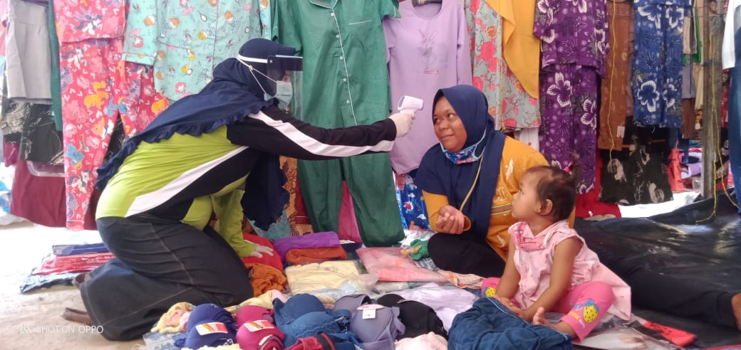 Petugas memeriksa suhu tubuh pedangan di pasar tradisional