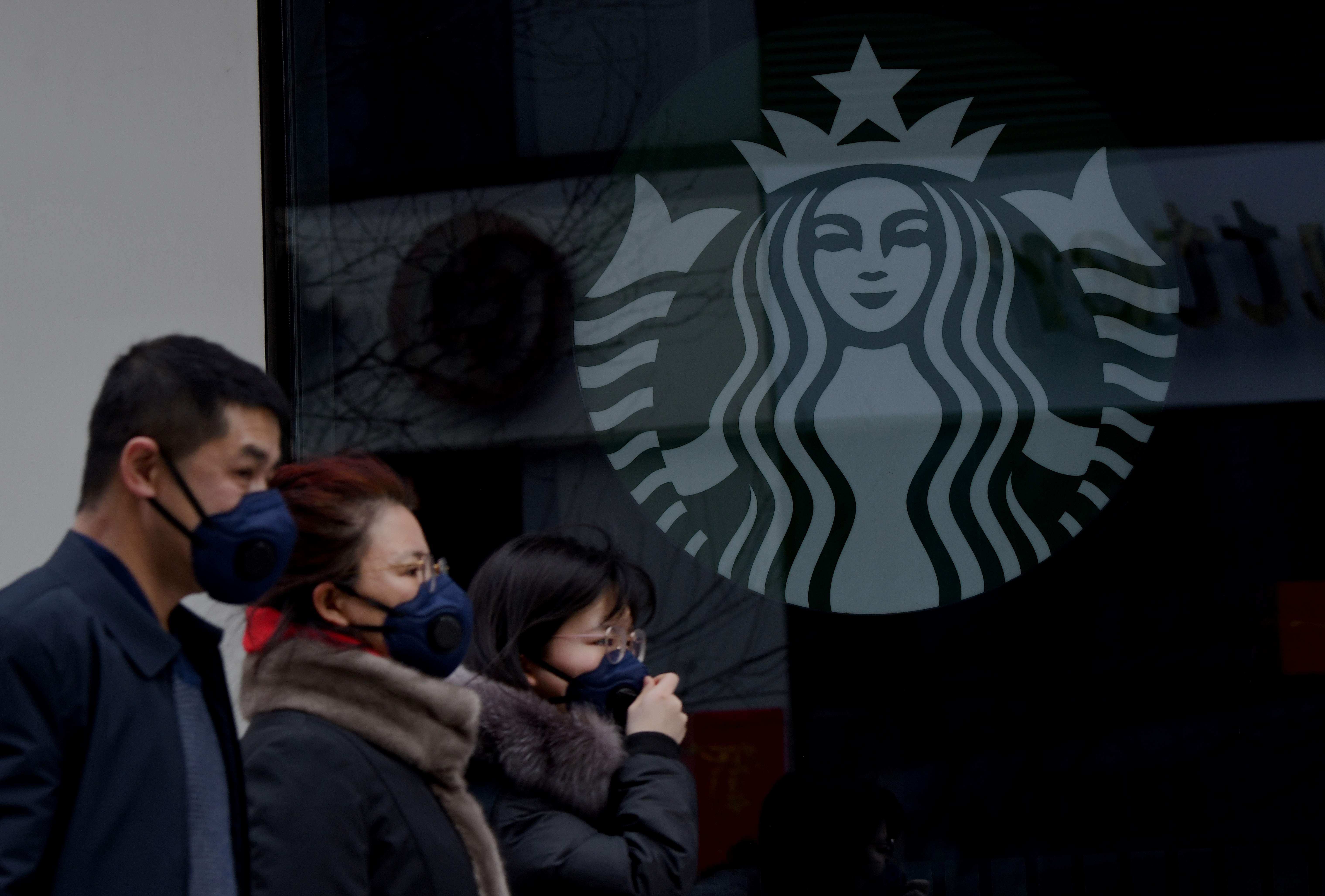 Orang-orang memakai masker melewati depan Starbucks
