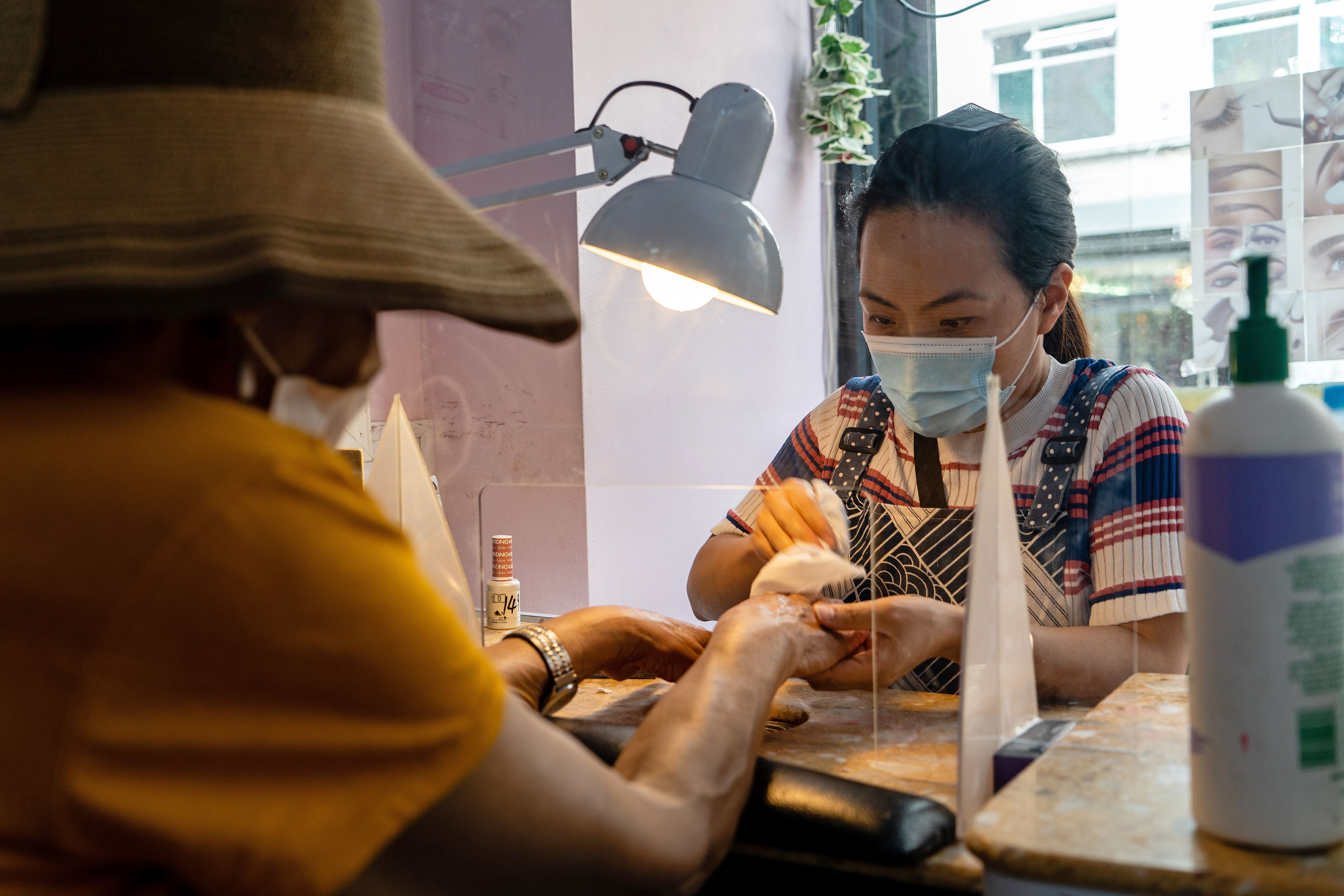 Seorang pekerja salon kuku mengenakan masker saat melayani kliennya di London, Inggris.