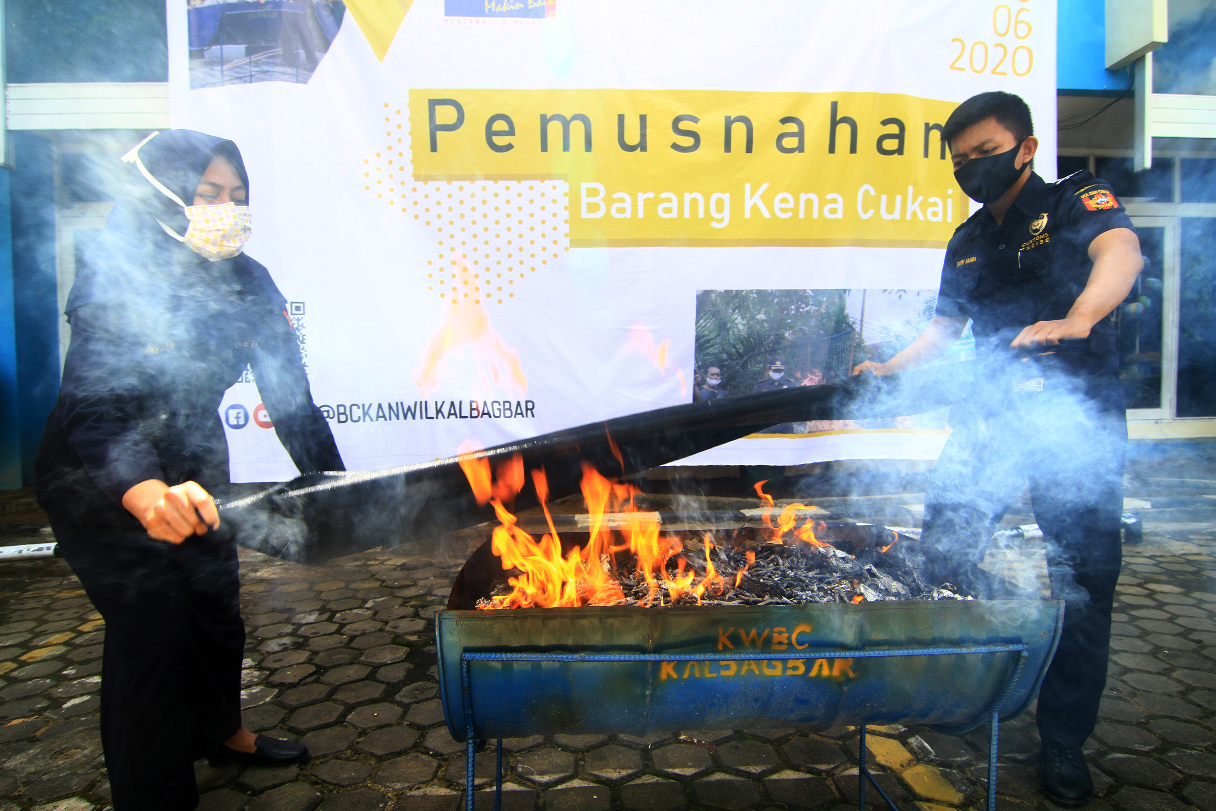  Dua petugas Bea Cukai membentangkan kain basah untuk memadamkan api yang telah membakar tumpukan rokok ilegal .