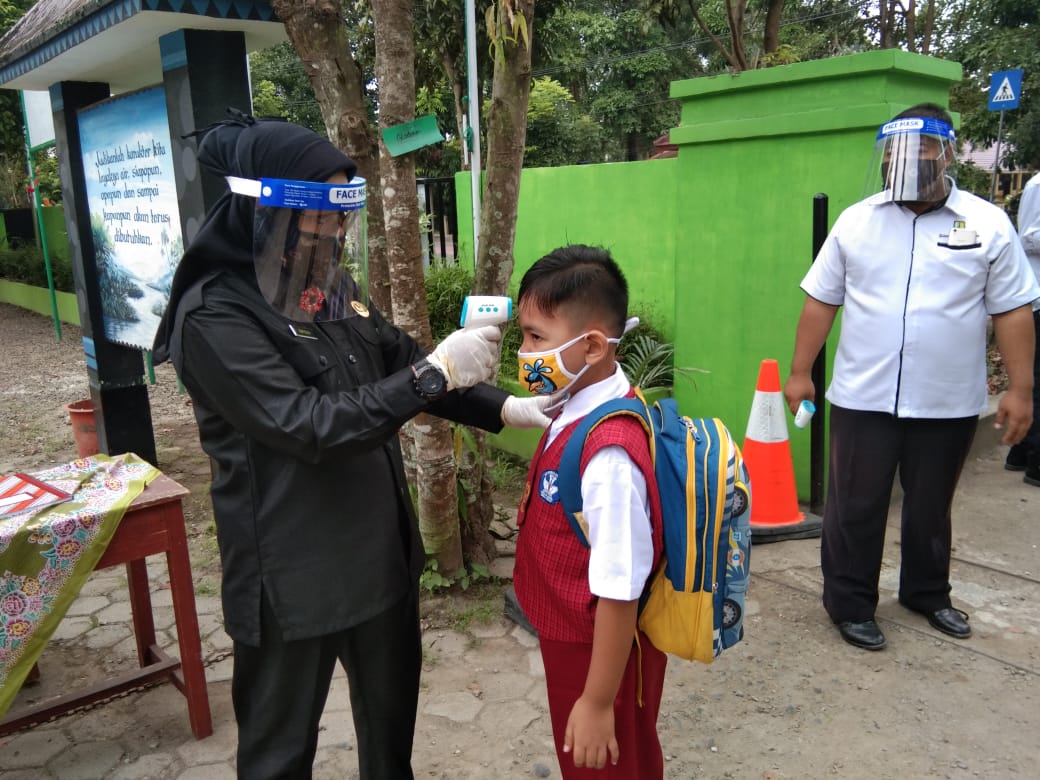 Seorang guru tengah memeriksa suhu tubuh seorang murid pada hari pertama masuk sekolah. 