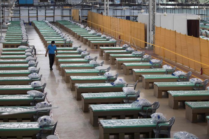 Pekerja berjalan di antara jejeran tempat tidur di aula sebuah kampus di New Delhi yang diubah menjadi tempat perawatan pasien Covid-19.