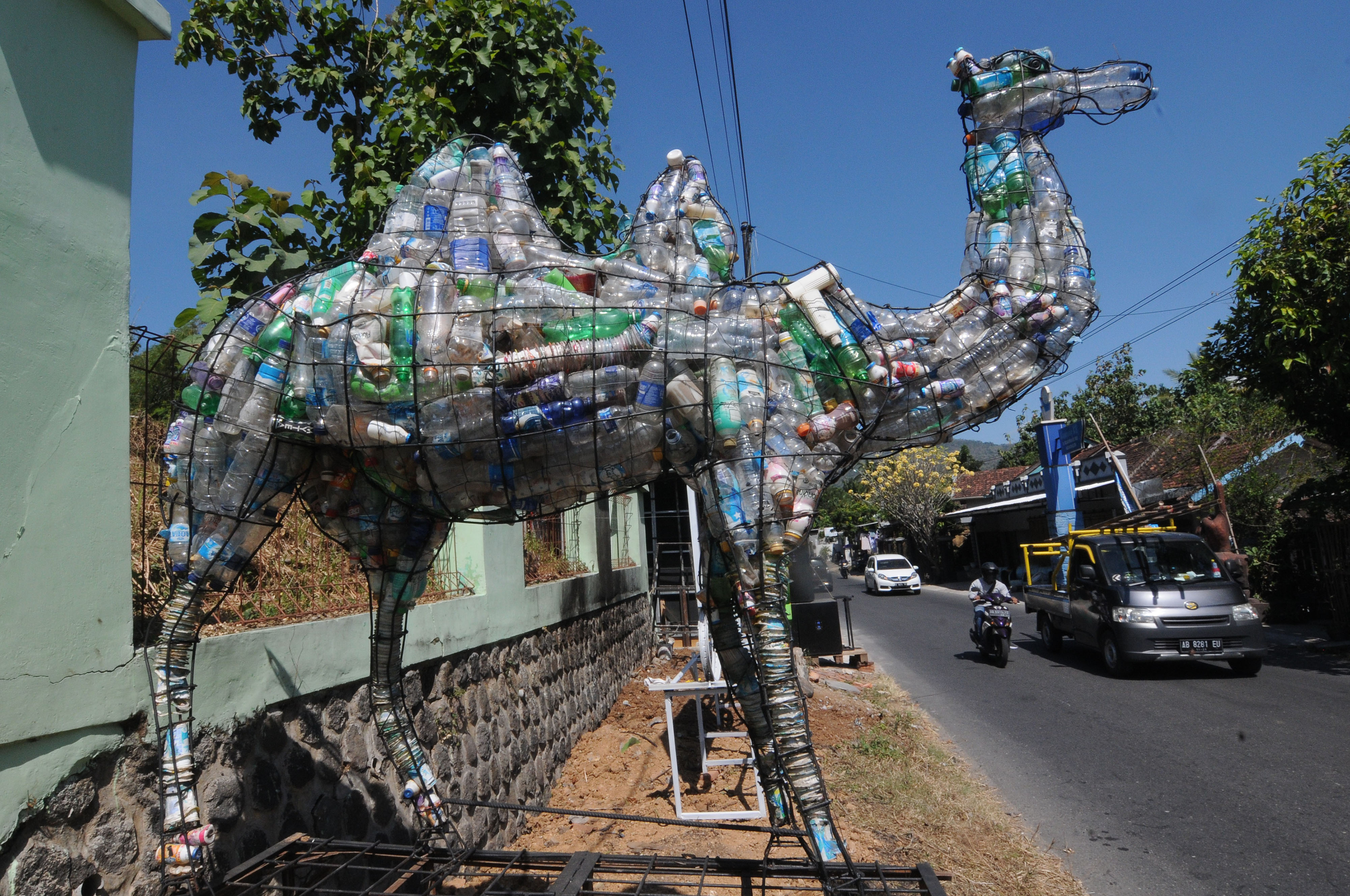 Sejumlah pengendara melintas di dekat ornamen unta yang terbuat dari susunan botol bekas yang dipajang dalam rangka Biennale Bank Sampah.