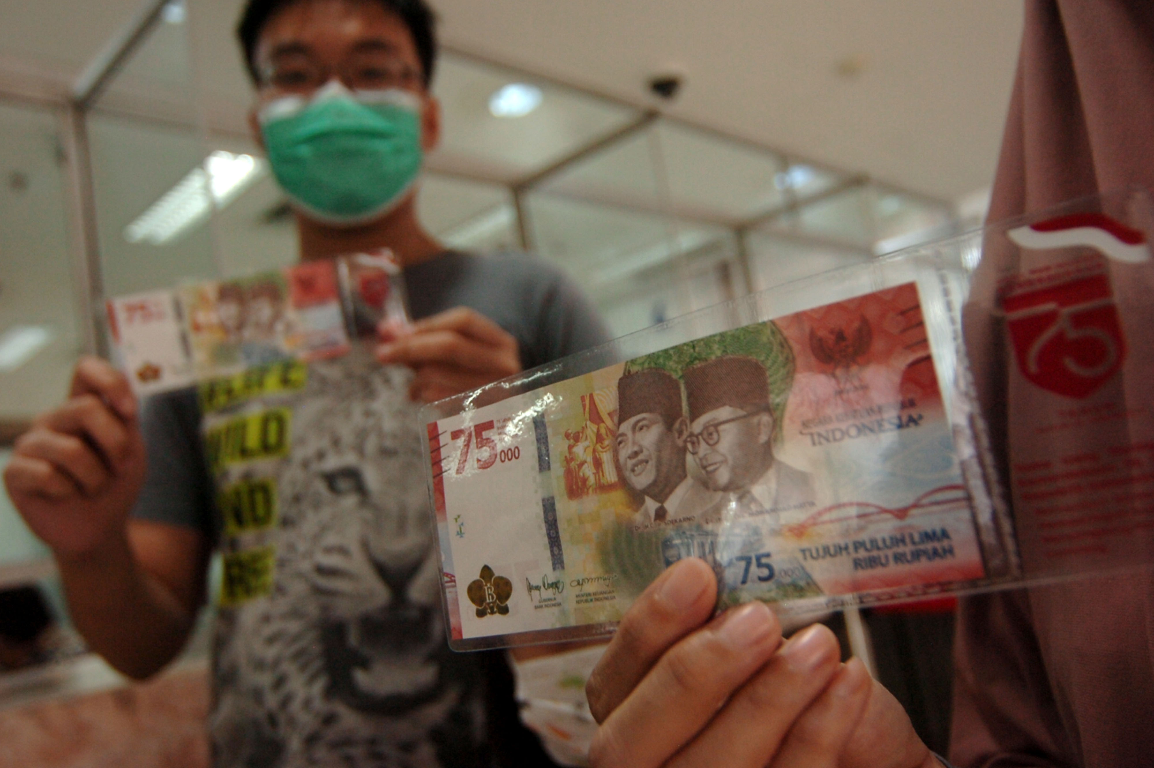 Masyarakat menunjukan uang Rp 75 ribu yang ditukarkan di Bank Indonesia. 
