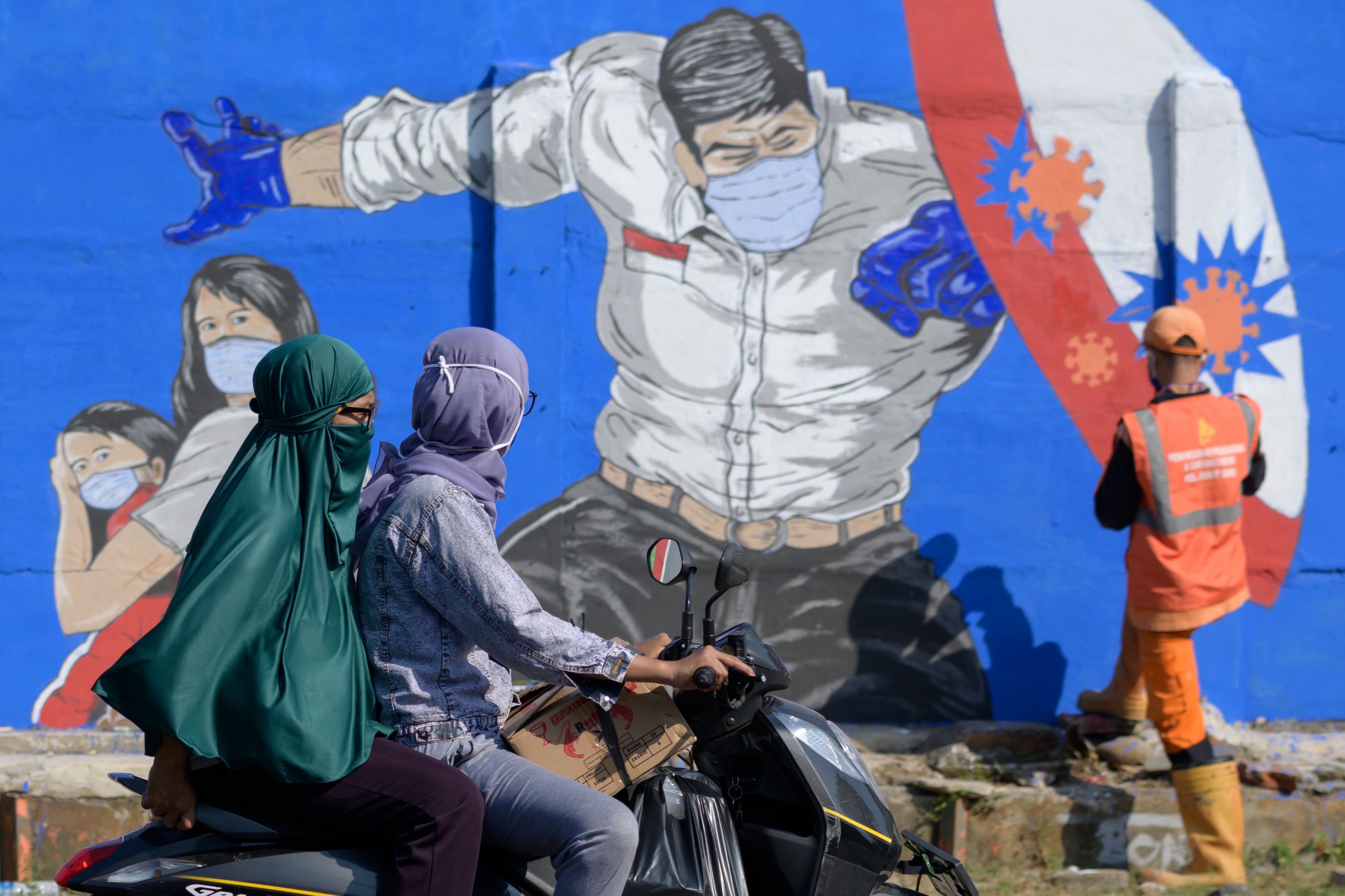 Pengendara melintasi mural covid-19 di wilayah Jakarta.