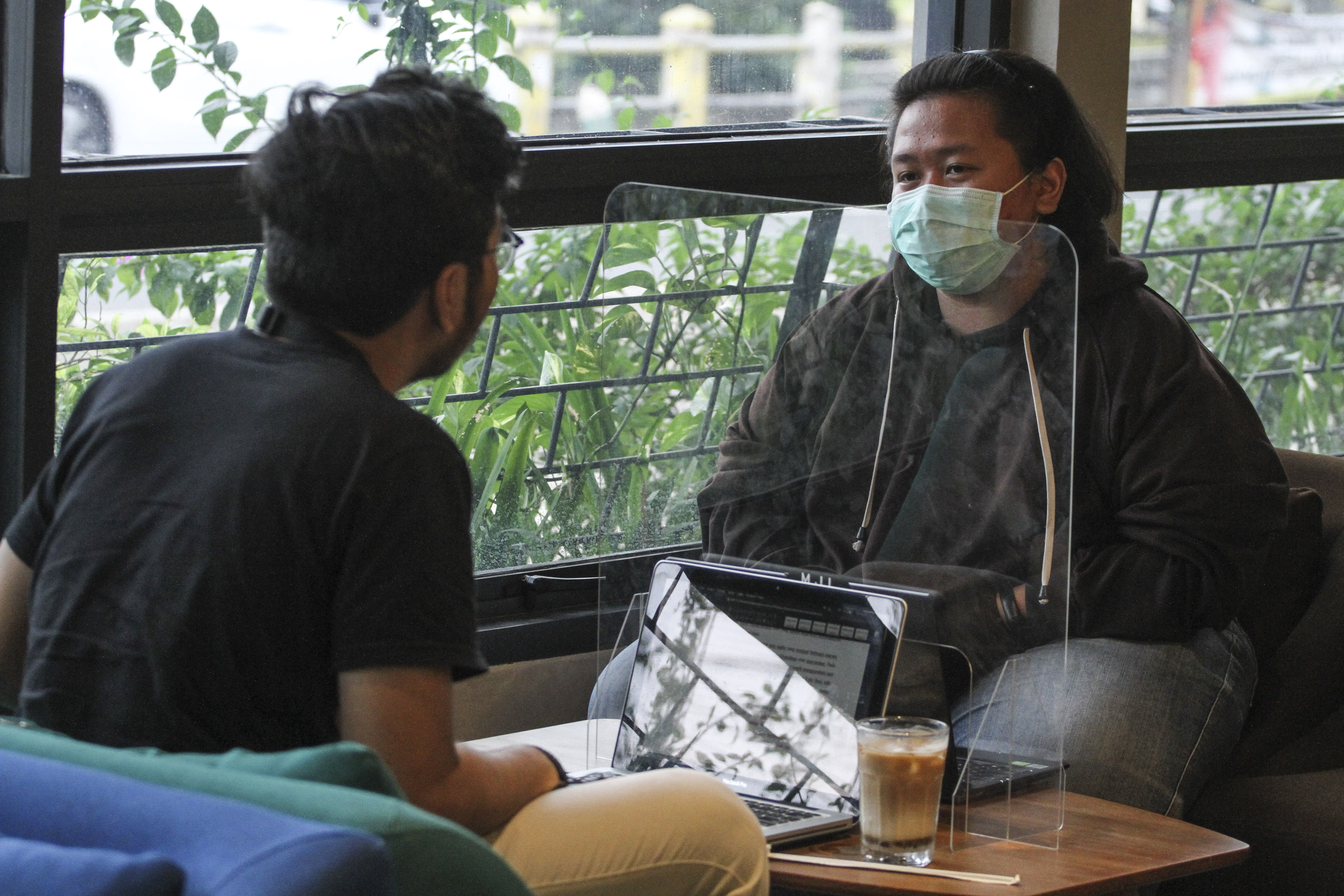 Pengunjung dengan sekat plastik duduk berjaga jarak di kedai kopi Mill Point, Depok, Jawa Barat.