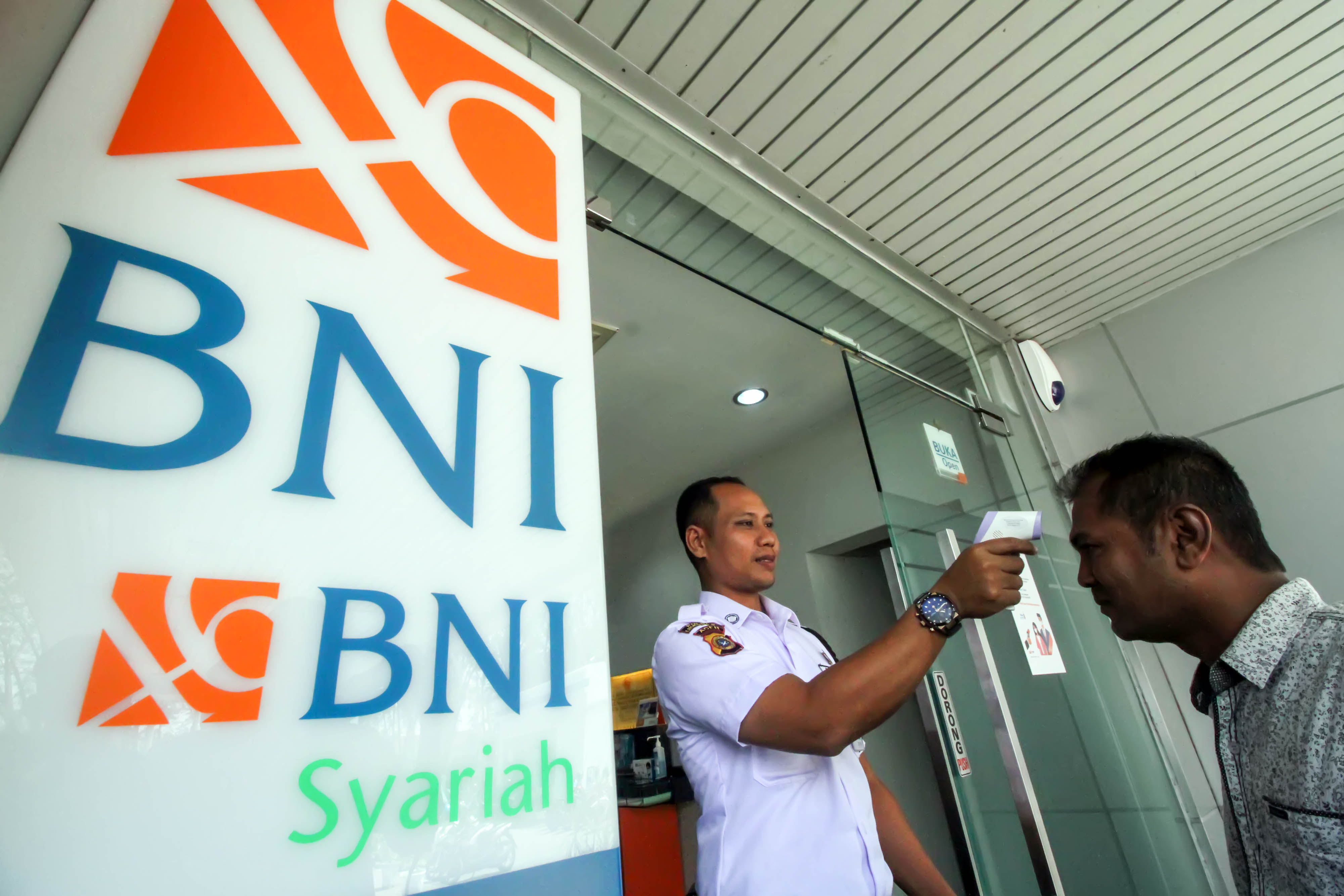 Petugas keamanan memeriksa suhu tubuh nasabah bank BNI Syariah Lhokseumawe, Aceh, Jumat (13/3).