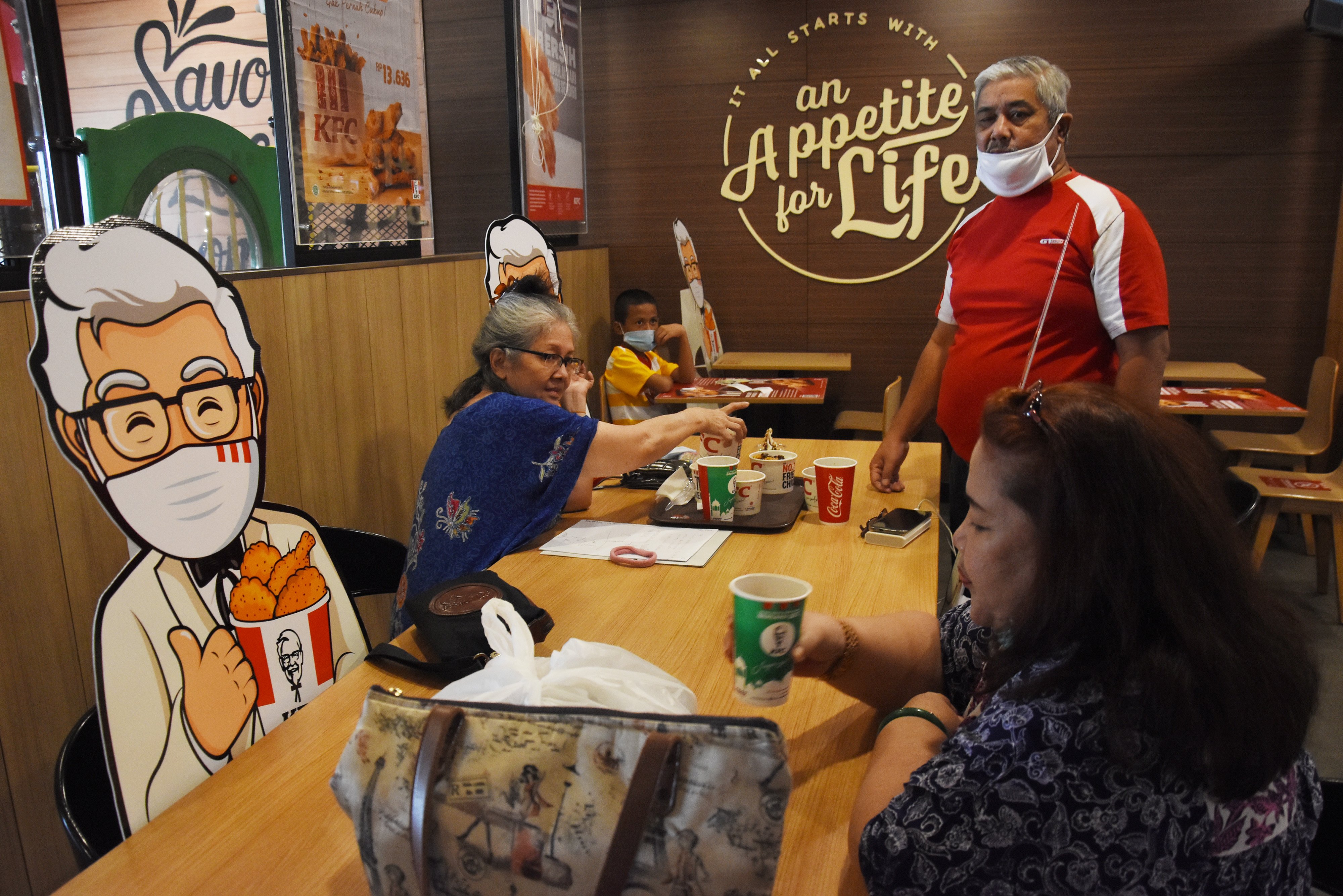 Pengunjung duduk di meja yang dipasangi mock-up maskot di salah satu restoran cepat saji di kawasan Tebet, Jakarta. 