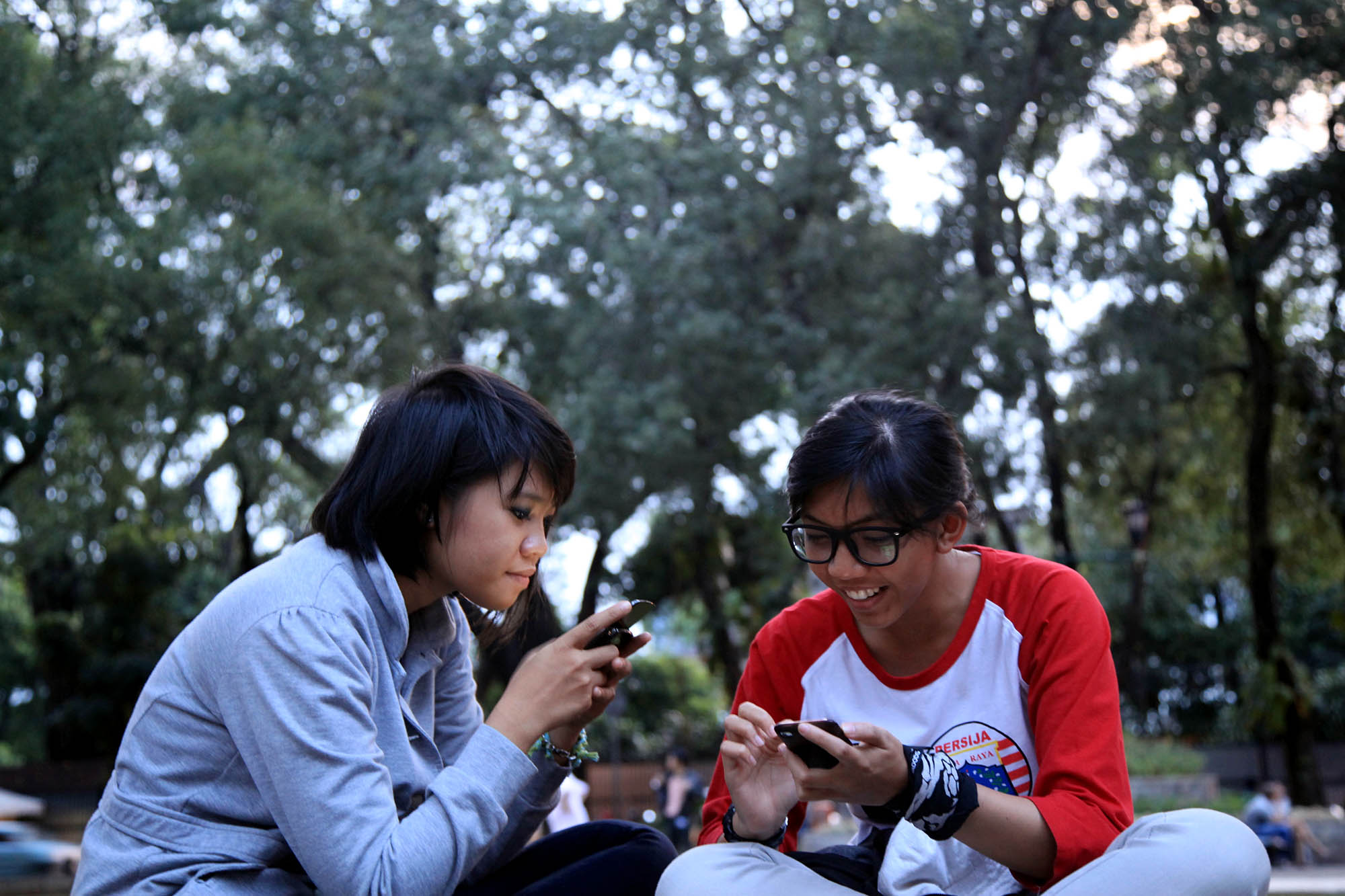 Dua warga berinternet menggunakan ponsel dengan memanfaatkan WIFI gratis di Taman Suropati, Menteng, Jakarta Pusat.