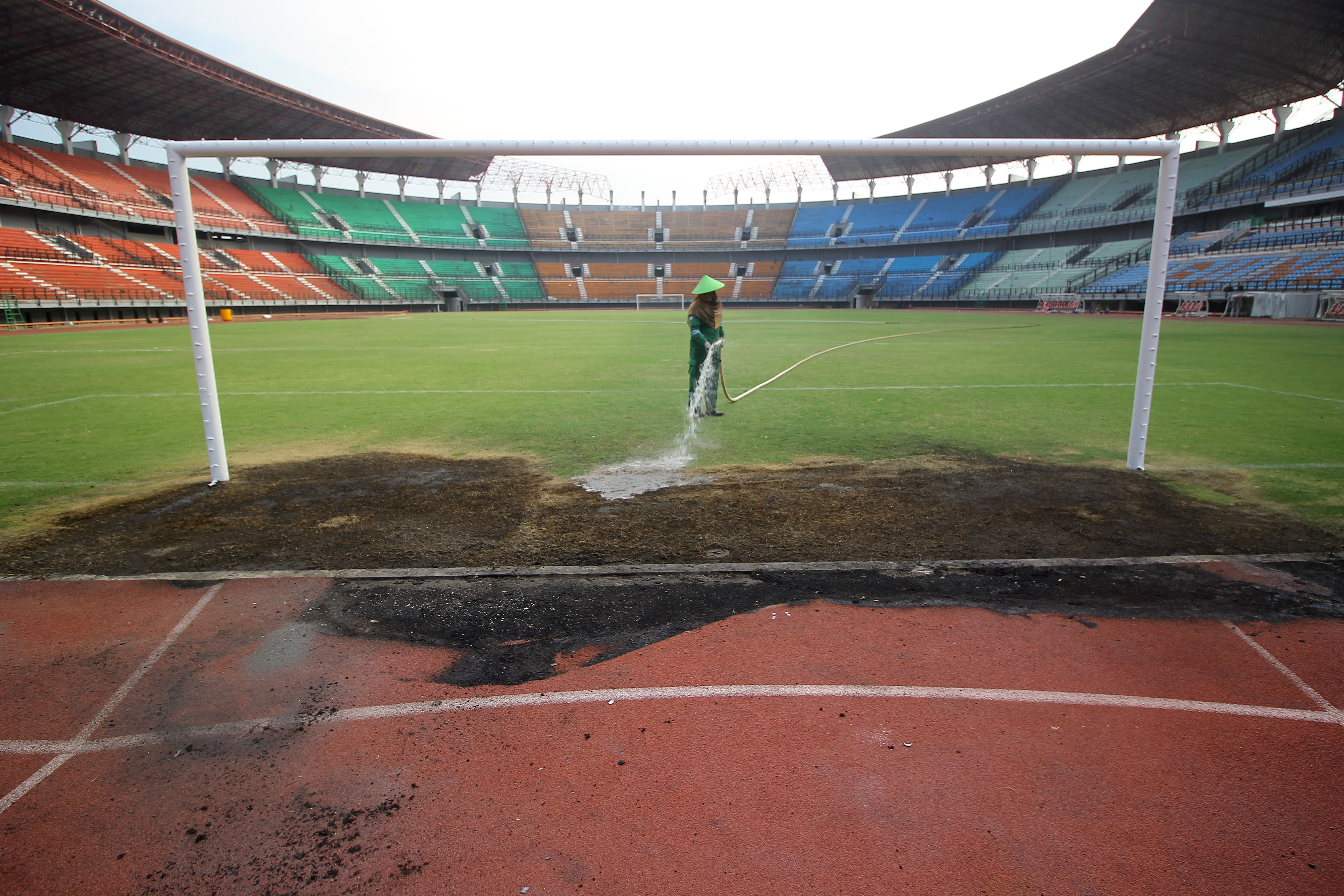 Pekerja menyiram bagian rumput Stadion GBT yang sempat dirusak suporter.