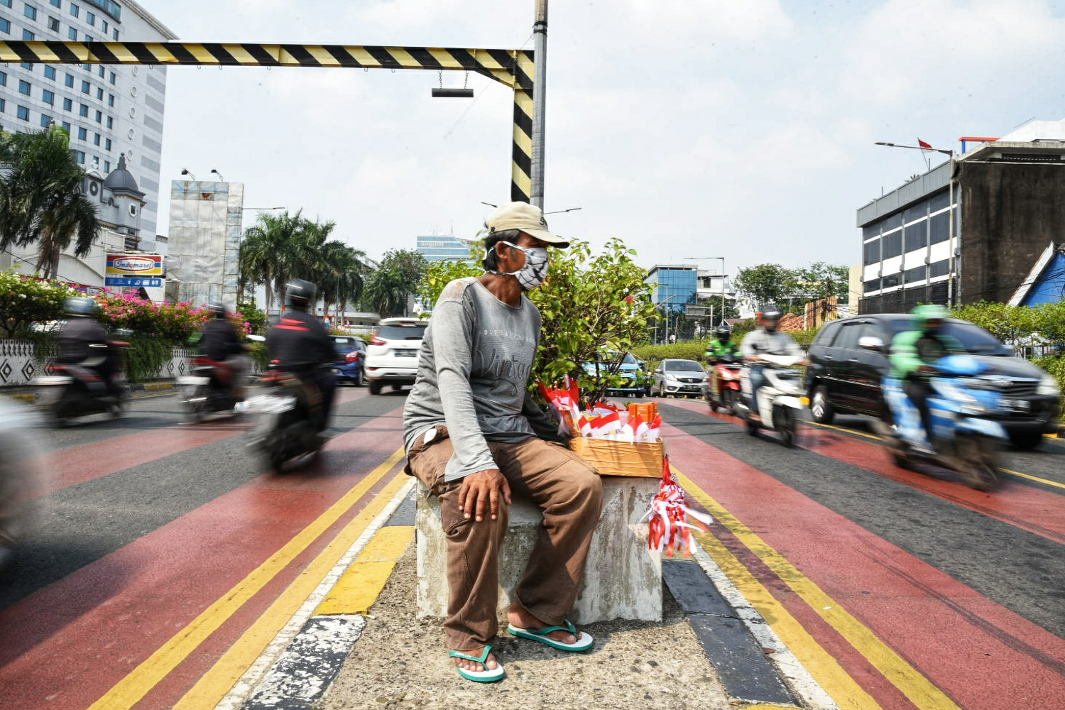 Seorang pedagang pernak pernik Hari Kemerdekaan duduk di tengah pembatas jalan.